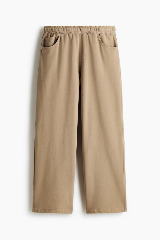 A pair of tan wide-leg pants is shown from the front, featuring an elasticated waistband and two slanted side pockets. The pants are cut straight with plain hems. - 1