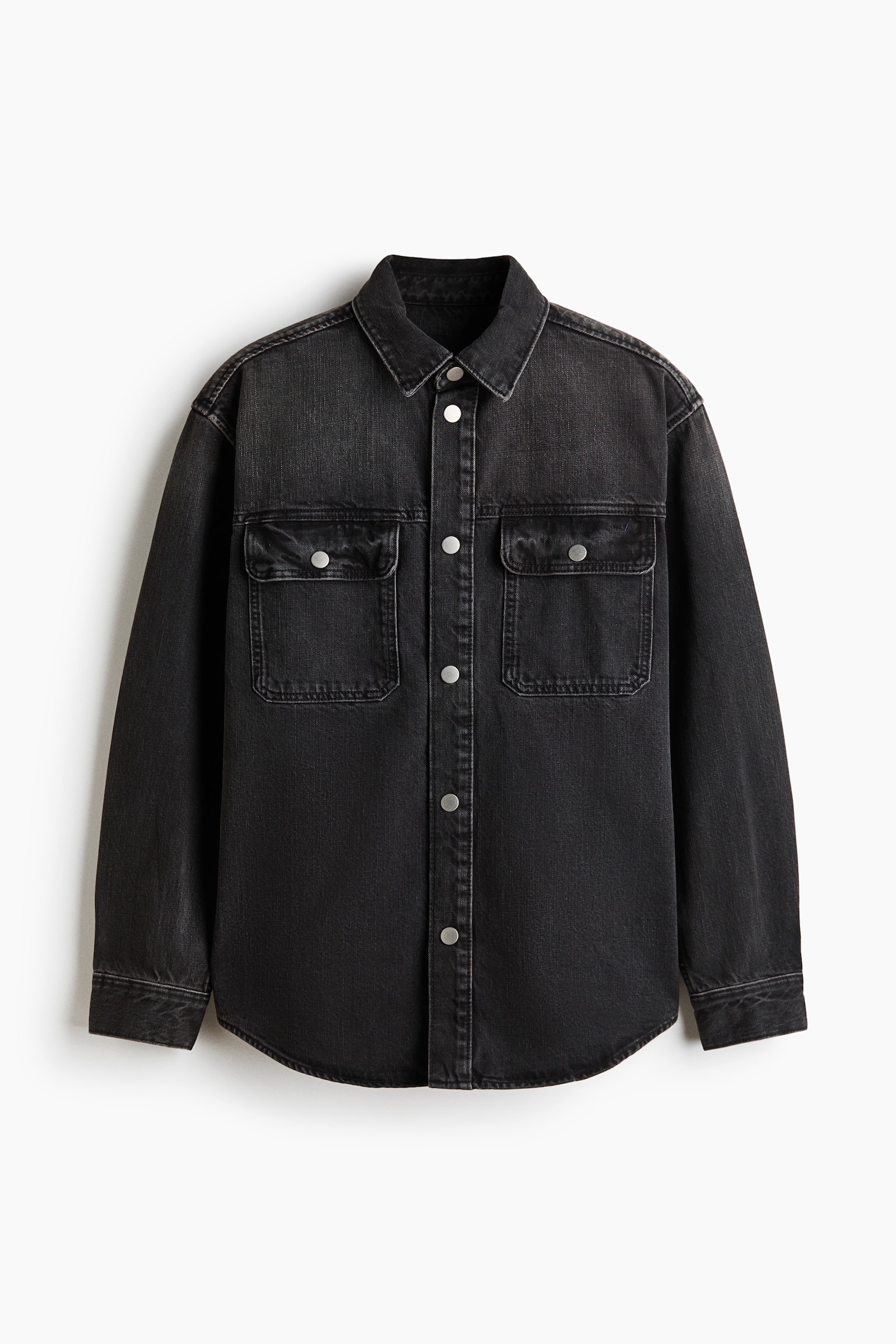 A washed black denim shirt is presenting its front view, featuring a classic pointed collar and a full snap button placket with silver-toned buttons. Two chest patch pockets with flaps and snap closures are visible, along with long sleeves ending in single snap button cuffs and a curved hem. - 1