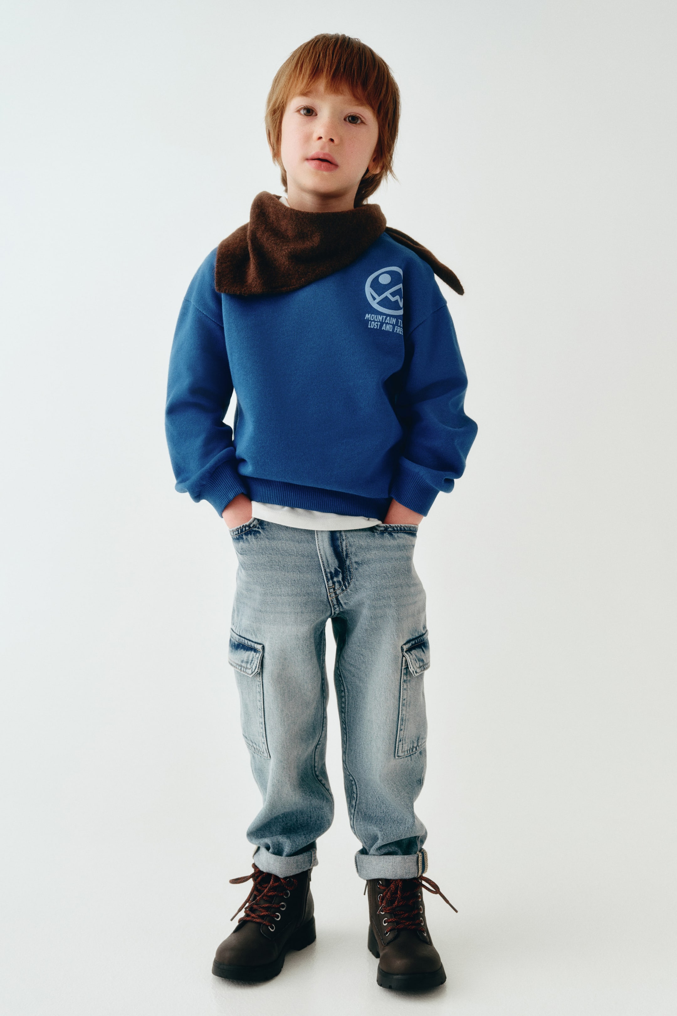 View larger image: Relaxed tapered-fit jeans in a light blue wash feature a front-facing relaxed silhouette with utility cargo pockets on the sides. The jeans are styled with rolled cuffs at the ankles, resting over dark lace-up boots, with hands tucked into the front slant pockets to highlight the casual fit.