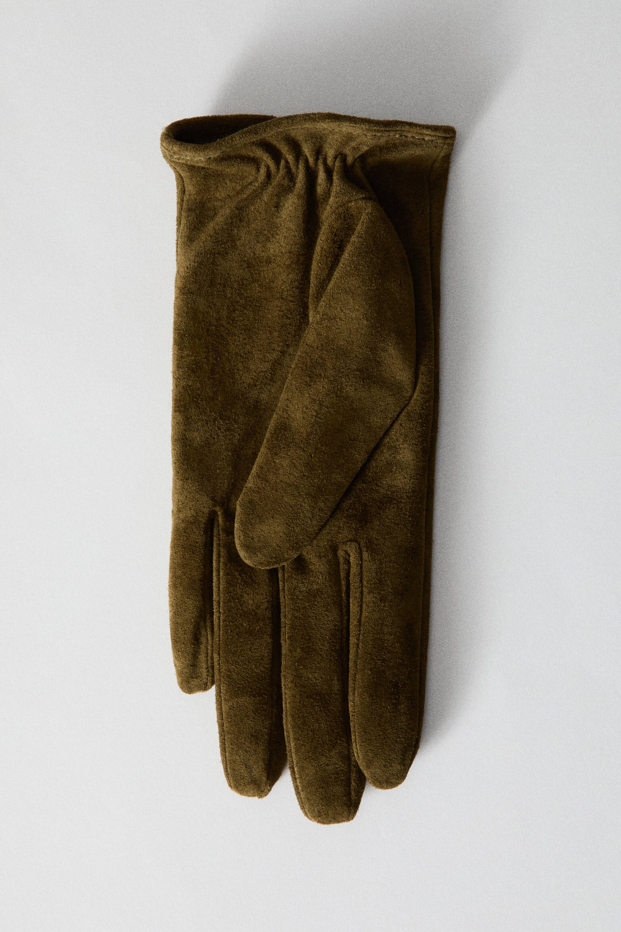Ver imagen más grande: Un par de guantes de ante verde oliva está colocado en posición plana, mostrando su textura suave y mate. El guante que queda en primer plano muestra un puño fruncido con elástico y el pulgar doblado.
