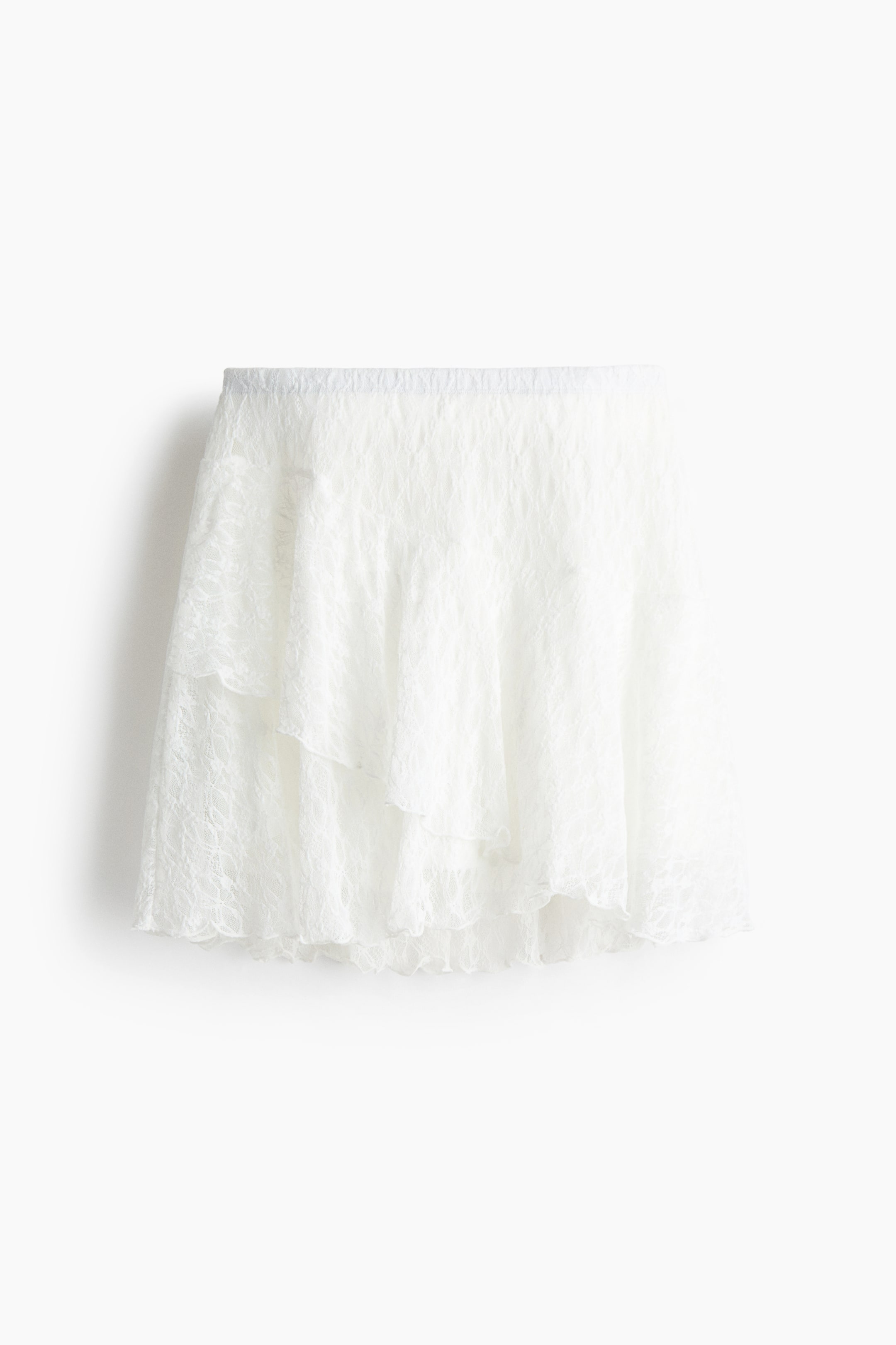 View larger image: "The white lace mini skirt is showcased from the front, highlighting several ruffled layers with scalloped edges and a dainty floral lace design throughout its sheer fabric."