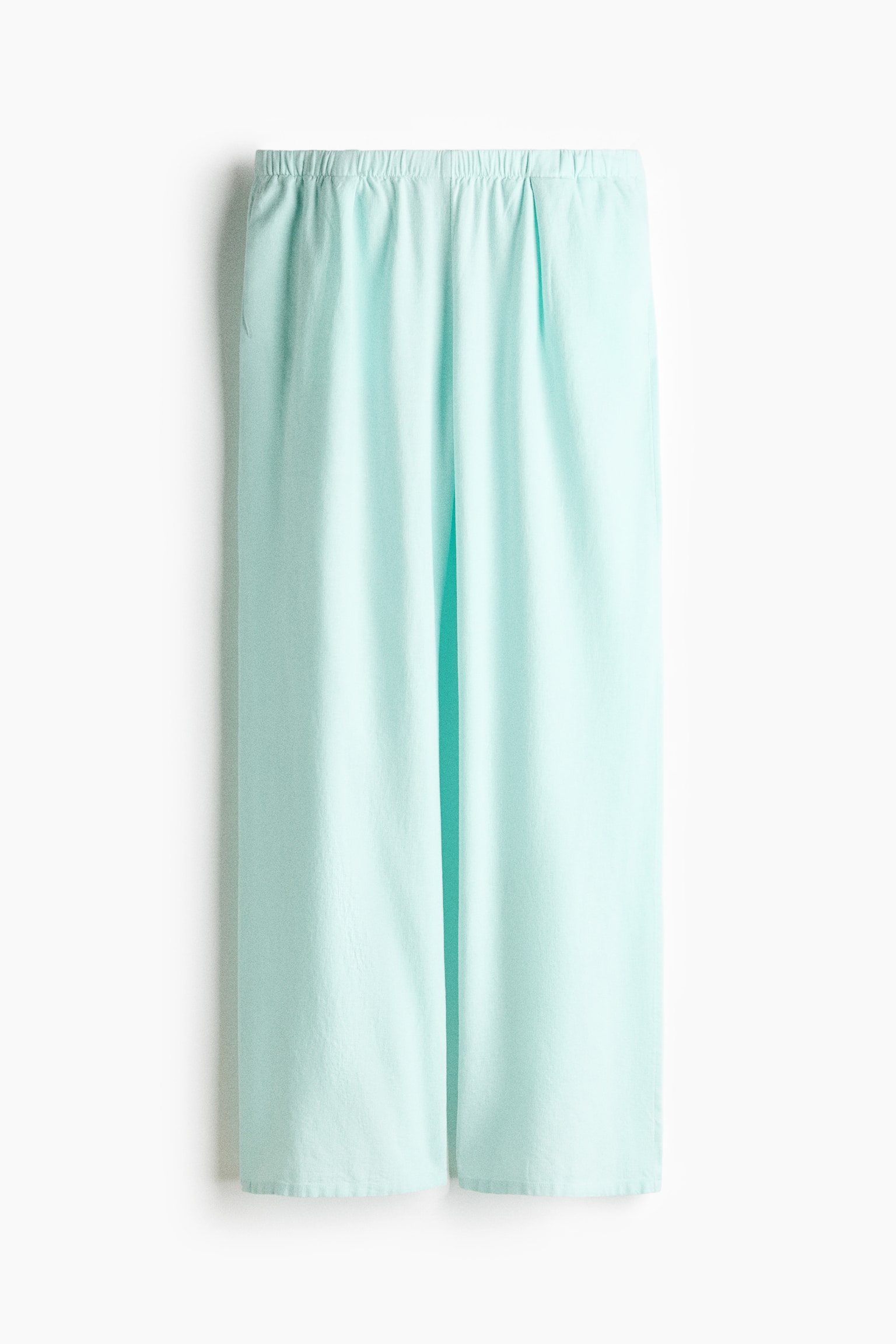 Light aqua trousers are facing front, featuring a loose fit and wide legs. They are presenting a low, elasticated waist showing gathers, discreet side pockets, and inverted box pleats at the top of the legs. - 1