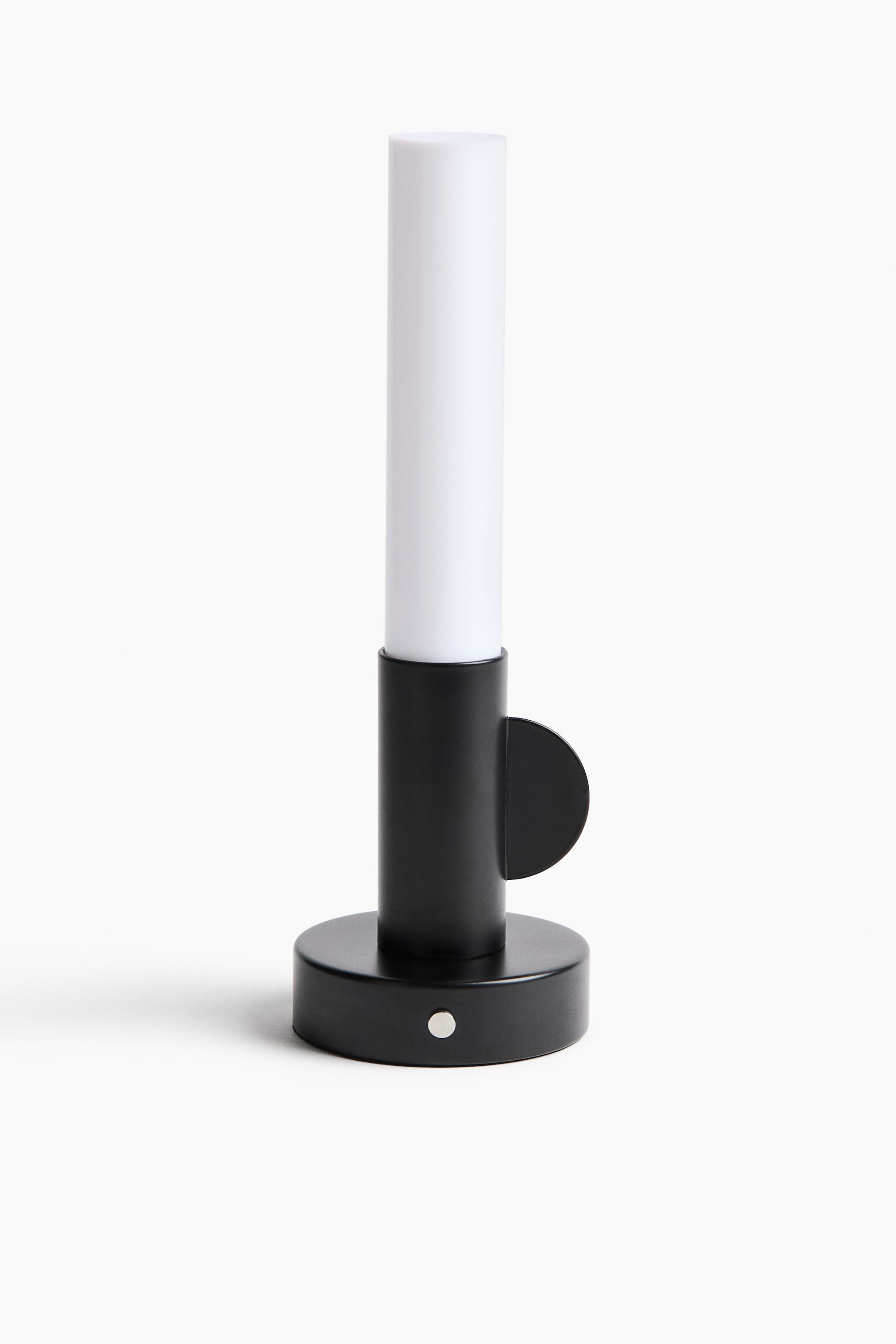 Grotere afbeelding bekijken: Een oplaadbare tafellamp toont zijn voorzijde, met een zwarte ronde voet en een zichtbare zilveren aan/uit-schakelaar. Een zwarte cilindrische kolom rijst op uit de voet en draagt een wit cilindrisch plastic bovenstuk, waarmee een kaarsachtig ontwerp ontstaat, inclusief een zwart halfrond detail dat vanaf de zijkant uitsteekt.