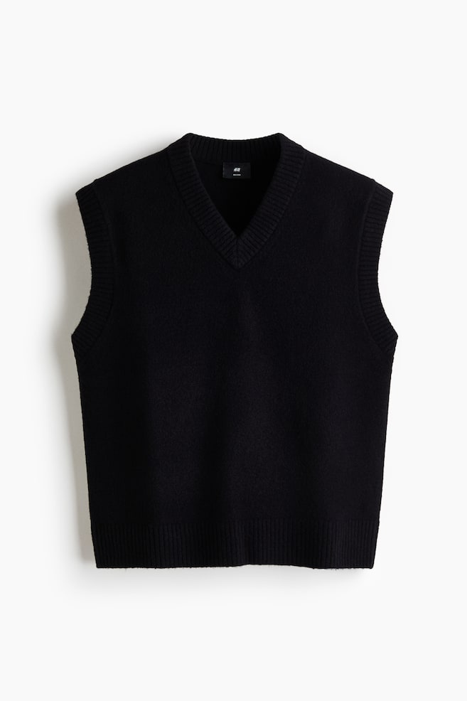 A black sleeveless sweater is facing front, featuring a V-neckline. It is presenting a subtle, textured knit with ribbed trim along the V-neck, armholes, and straight bottom hem. - 1