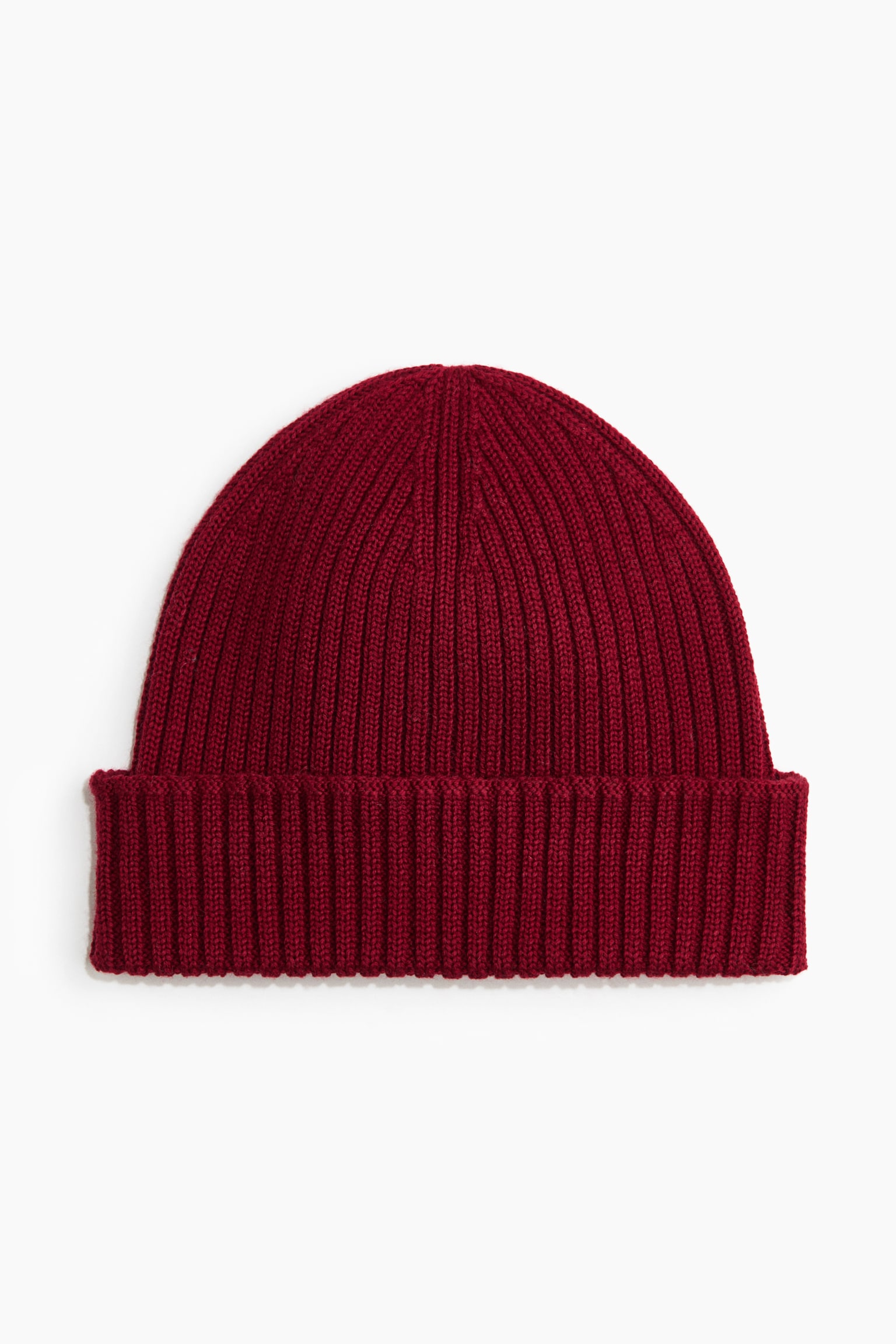 A deep red rib-knit beanie is shown front-on, featuring a thick folded-up cuff and a rounded crown with a consistent vertical ribbed pattern.