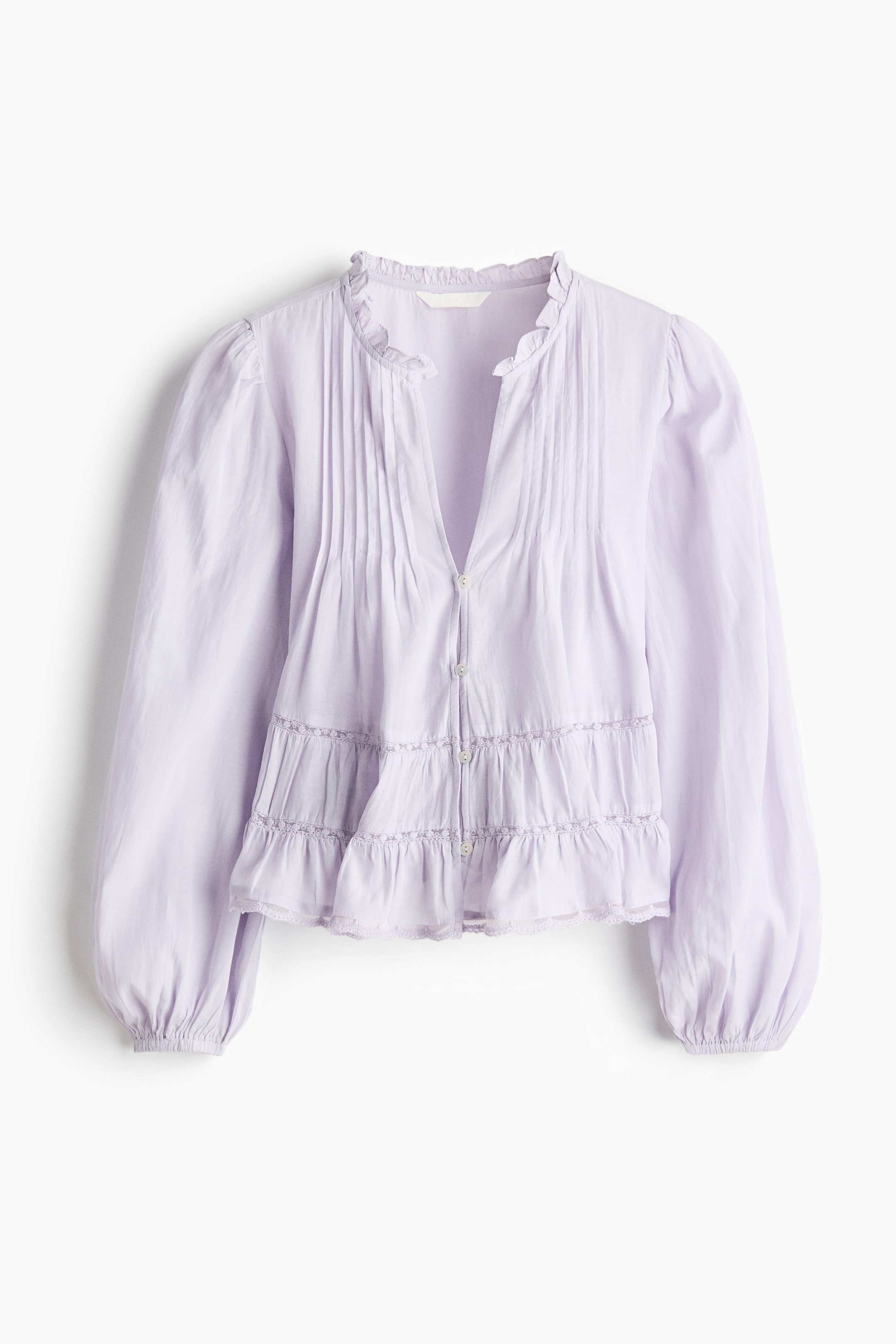 View larger image: A short lilac blouse in a viscose and cotton weave is shown from the front, featuring a frilled collar, pintucks at the front, a V-neckline, and buttons running down the front. It displays long balloon sleeves with elasticated cuffs, and gathered tiers with narrow lace insets appear above the hem.