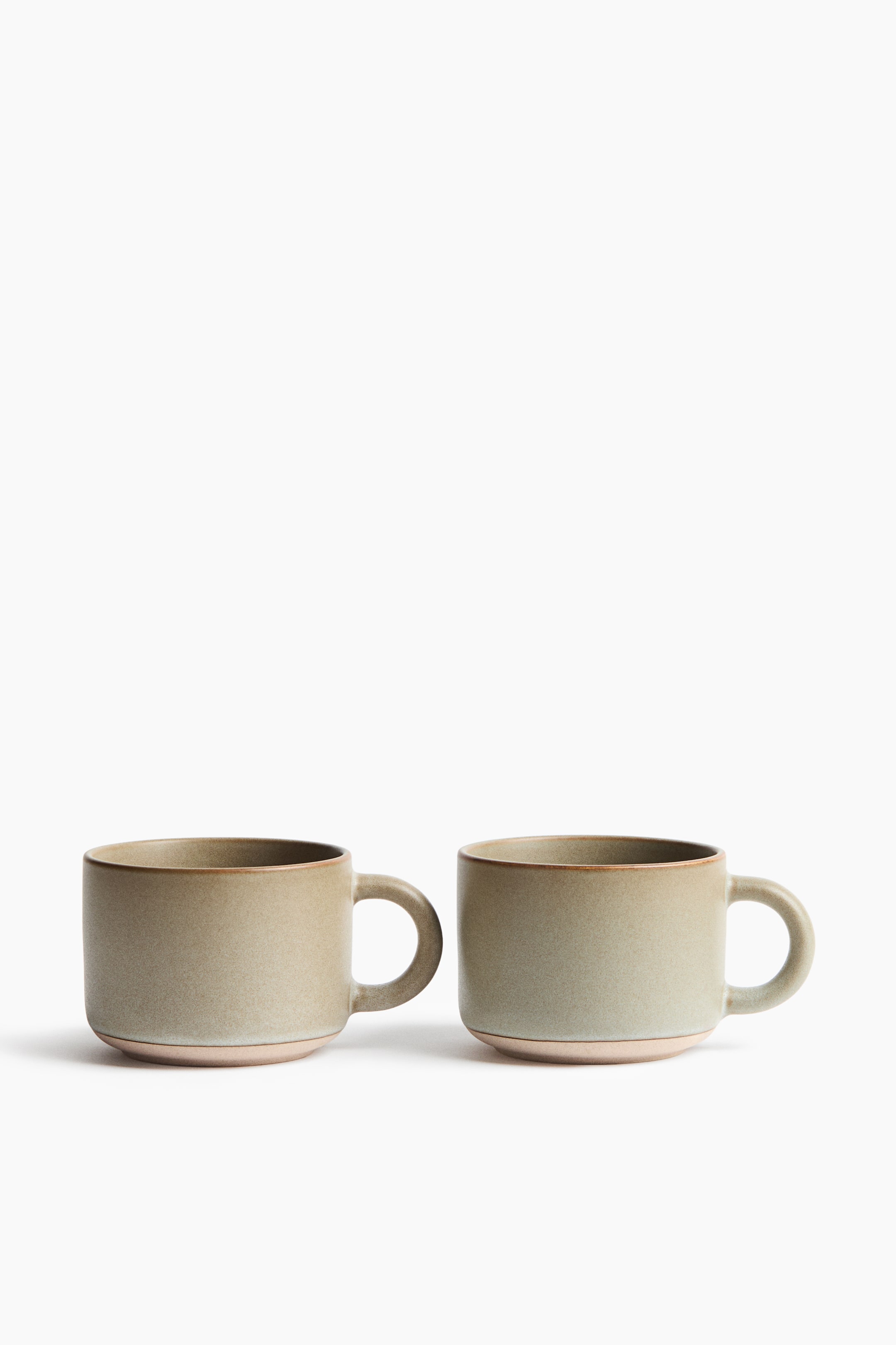 View larger image: Two ceramic mugs showcase a dusty green glazed finish, complemented by a dark brown rim and an unglazed light tan base. Each mug is designed with a C-shaped handle.