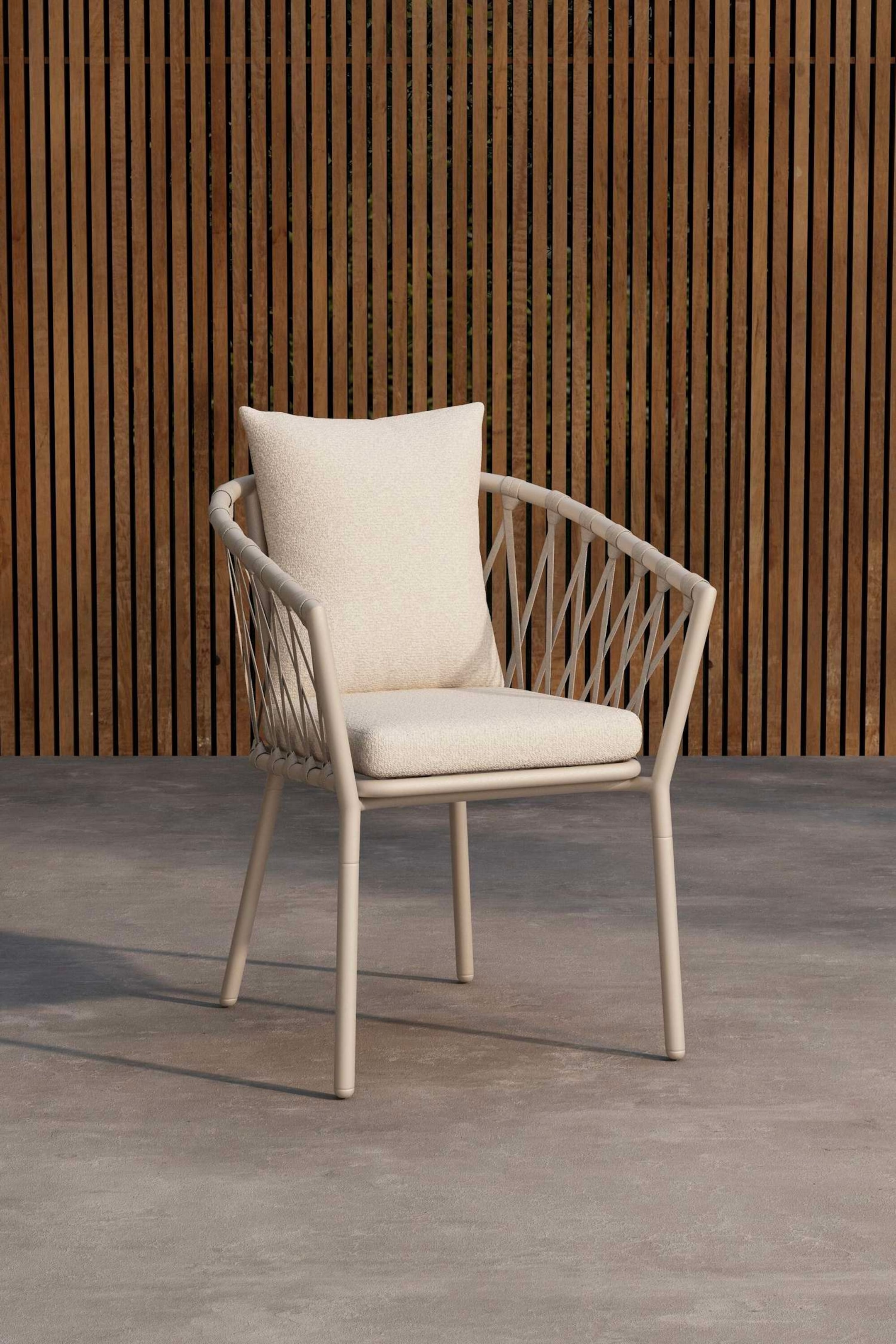 Agrandir l'image: Un fauteuil d'extérieur est positionné légèrement en biais, orienté vers l'avant et vers la gauche. Il présente une structure de couleur beige clair avec des cordages tressés formant le dossier et les côtés ouverts, et des coussins de siège et de dossier texturés de couleur crème y reposent.