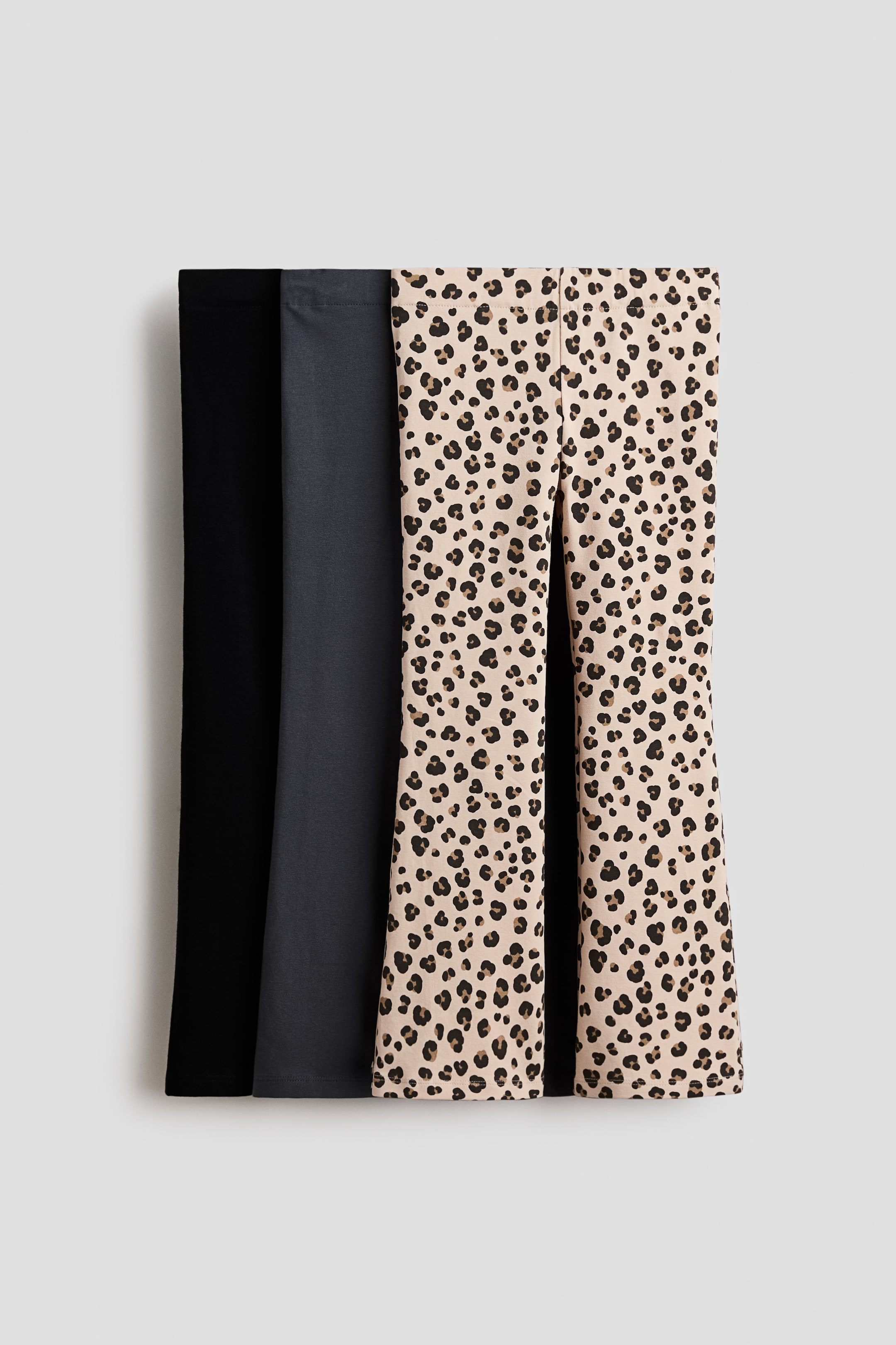 View larger image: Three pairs of jersey leggings are presenting from the front, showing elasticated waists and flared legs. They are featuring one black pair, one dark gray pair, and one beige pair with a black and brown leopard print.