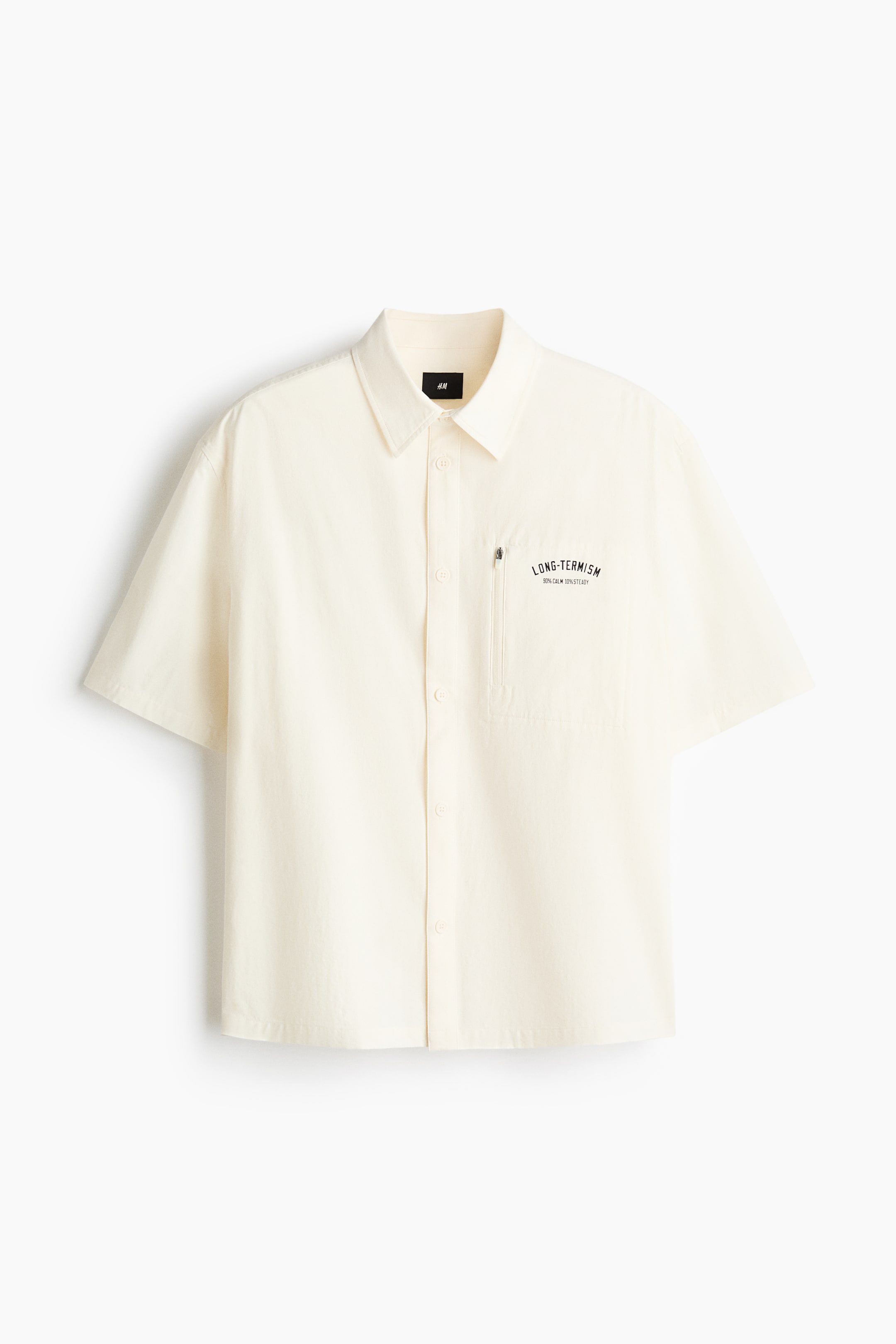 查看大圖: 短袖奶油色襯衫正面展示,配有翻領與經典鈕扣前襟,左胸有一個拉鍊胸袋,胸袋上方印有黑色字樣「LONG-TERMISM」及「90% CALM 10% STEADY」。這件棉質織物襯衫以直下擺收邊,呈現寬鬆剪裁。