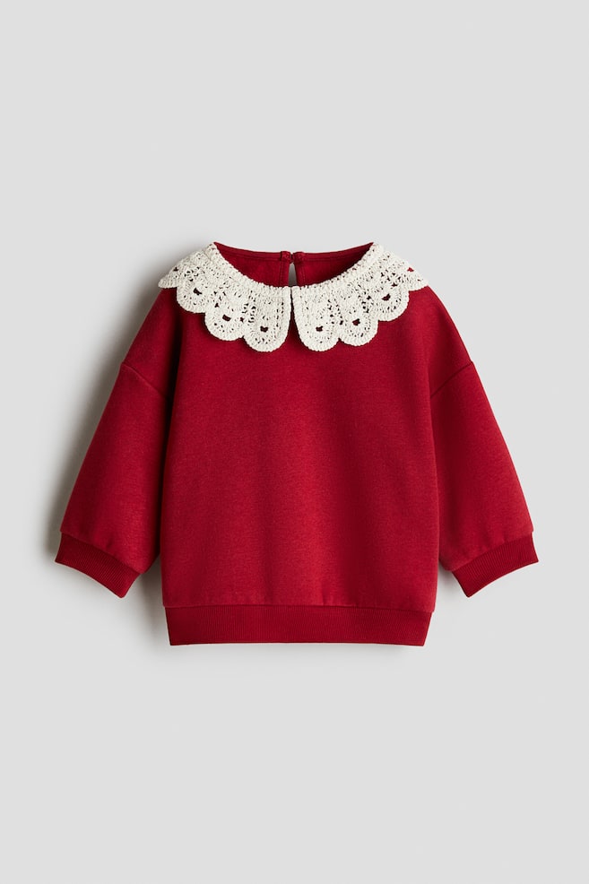 Uma camisola vermelha está a exibir a sua FRENTE, apresentando uma grande gola Peter Pan de renda branca e recortada. É desenhada com punhos canelados e uma bainha canelada. - 1