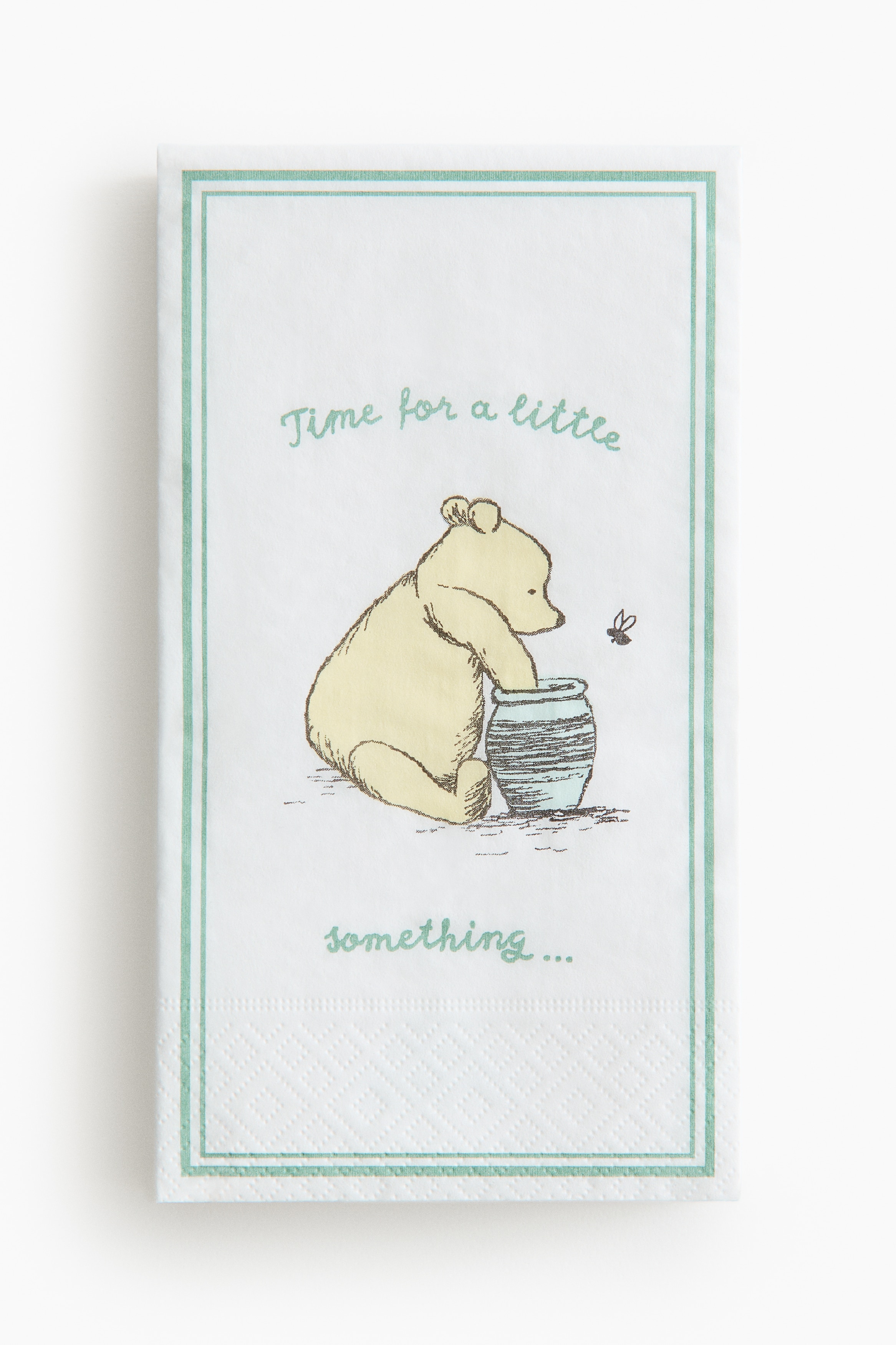 Ett Nalle Puh-matsalsset innehåller en vit mugg med grön kant och karaktärsillustration, en vit tallrik med grön kant och en detaljerad picknickscen, en hög vita servetter med grön kant och en Puh med honungsburk-illustration, samt en vit skål med grön kant.