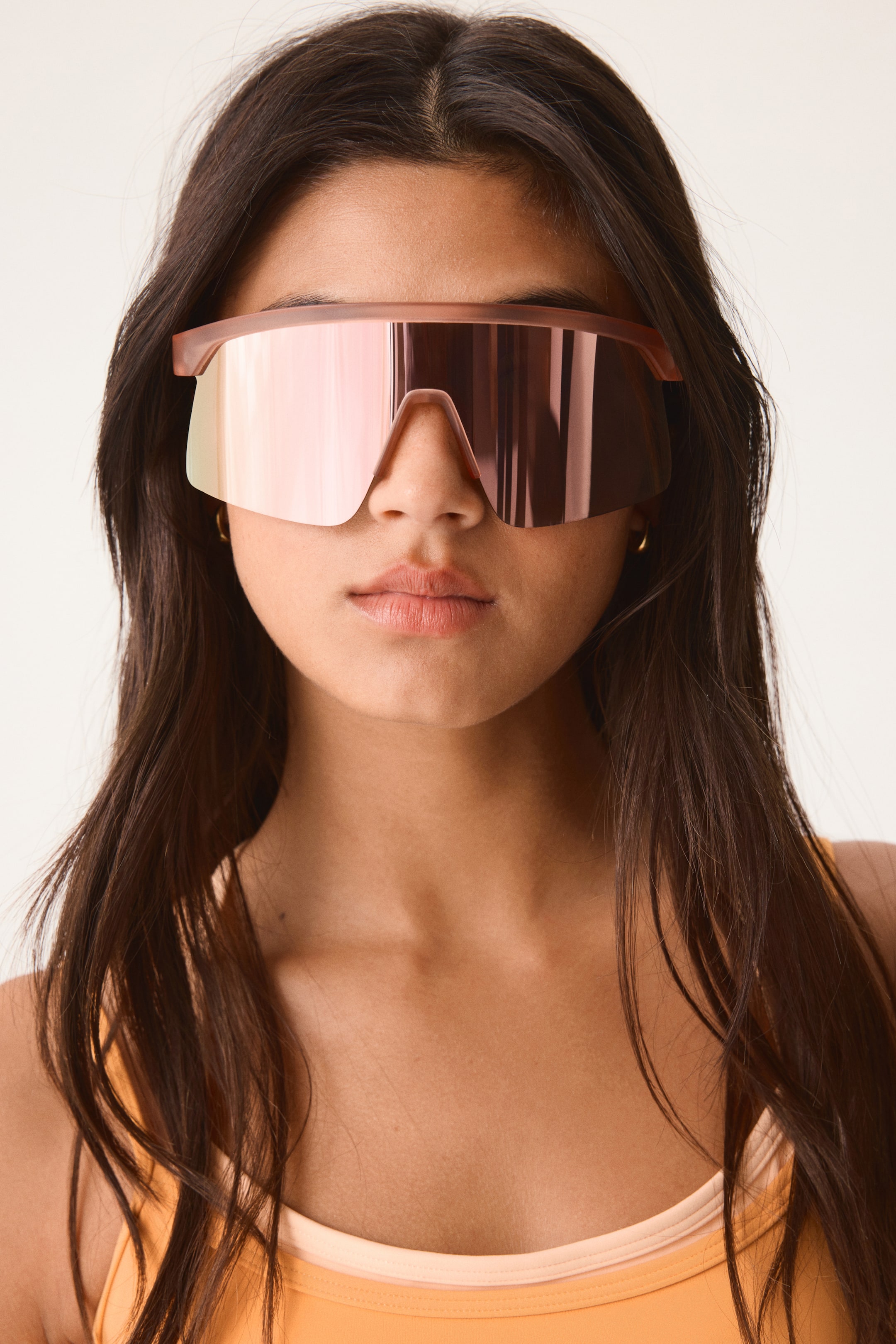 View larger image: These sunglasses showcase a large, single shield lens with a rose gold mirrored finish, viewed from the front. The top frame is a matte, translucent pinkish-brown, seamlessly integrating into the lens and extending across the brow.
