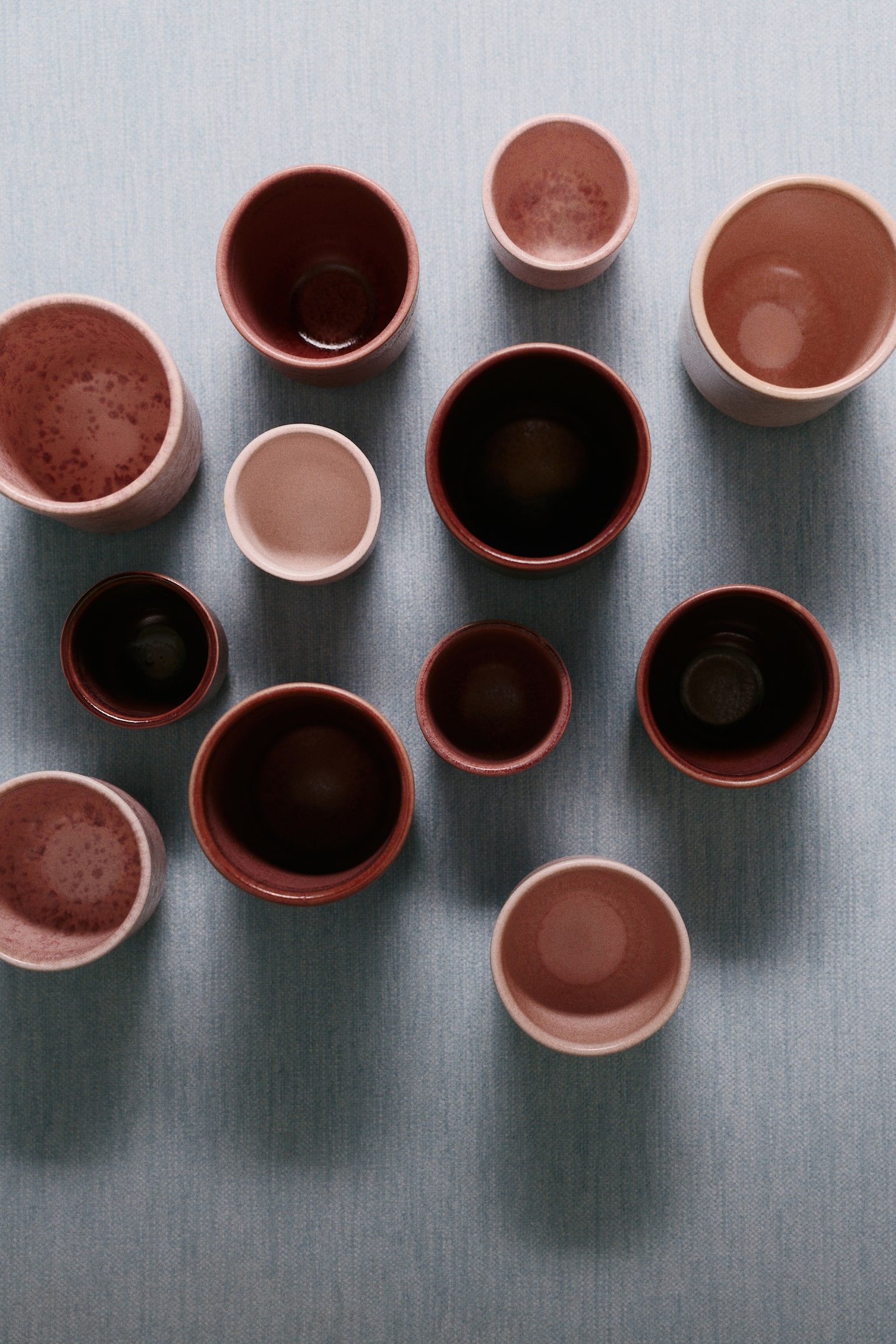 Stoneware espresso cups are arranged in a row from a front angle, showcasing a gradient of pink to deep mauve hues. Each cup displays a unique glazed finish, ranging from a smooth matte light pink to speckled and textured finishes. - 1