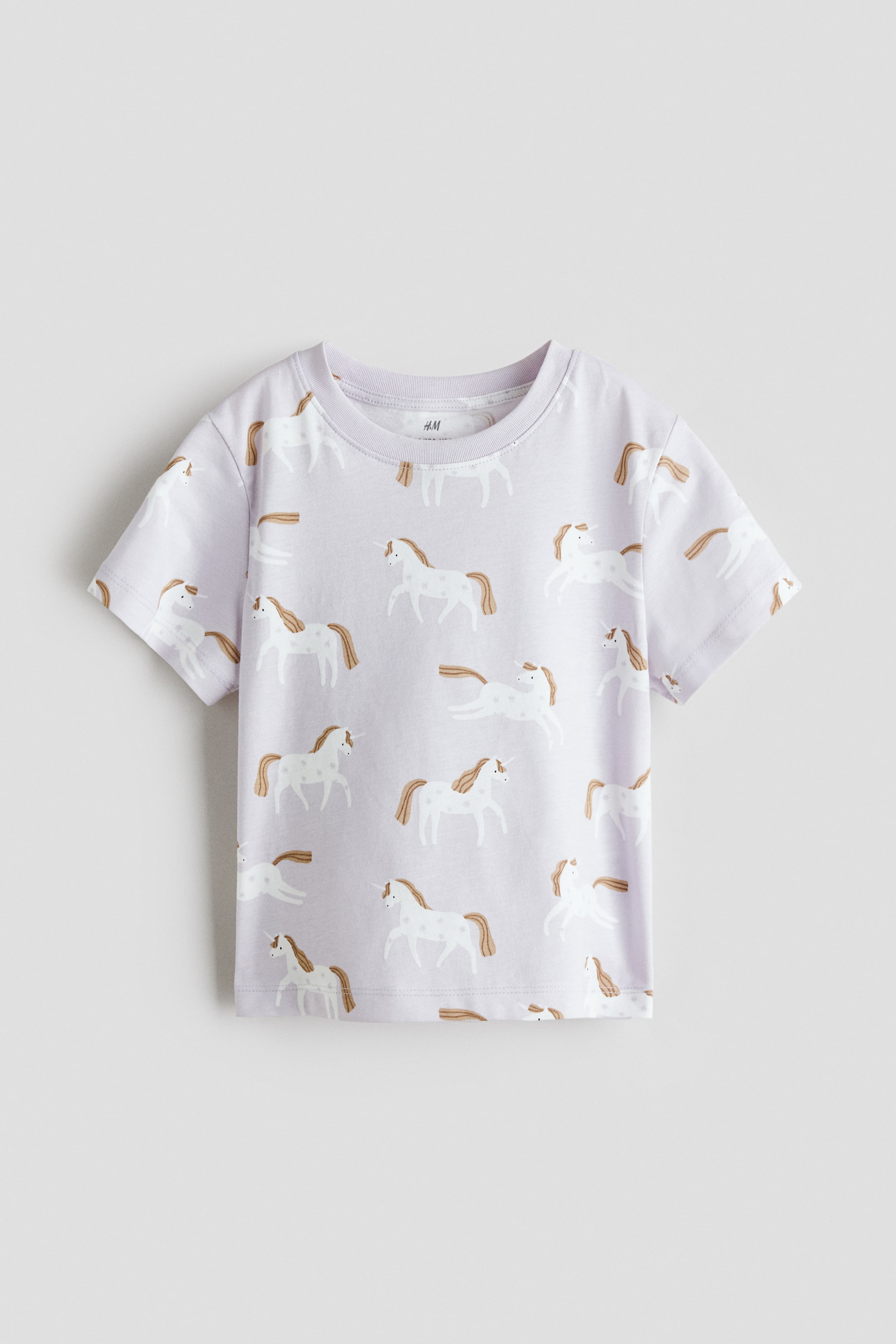 View larger image: The light purple t-shirt showcases a repeating pattern of white unicorns with brown manes and tails, featuring a crew neck and short sleeves.