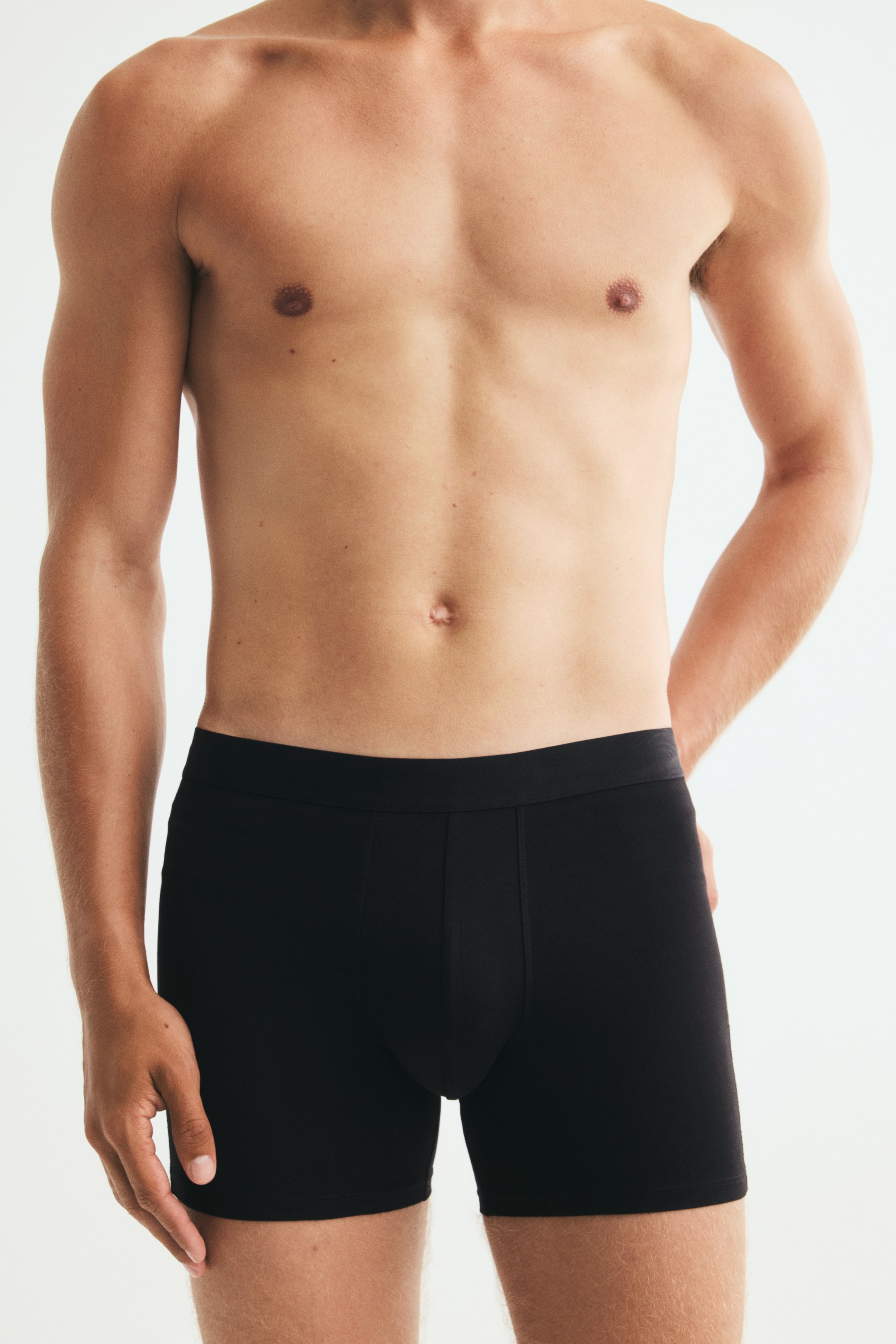 Agrandir l'image: Le mannequin porte un boxer noir à large ceinture plate. Ce sous-vêtement ajusté présente un panneau frontal galbé et descend jusqu’à mi-cuisse.