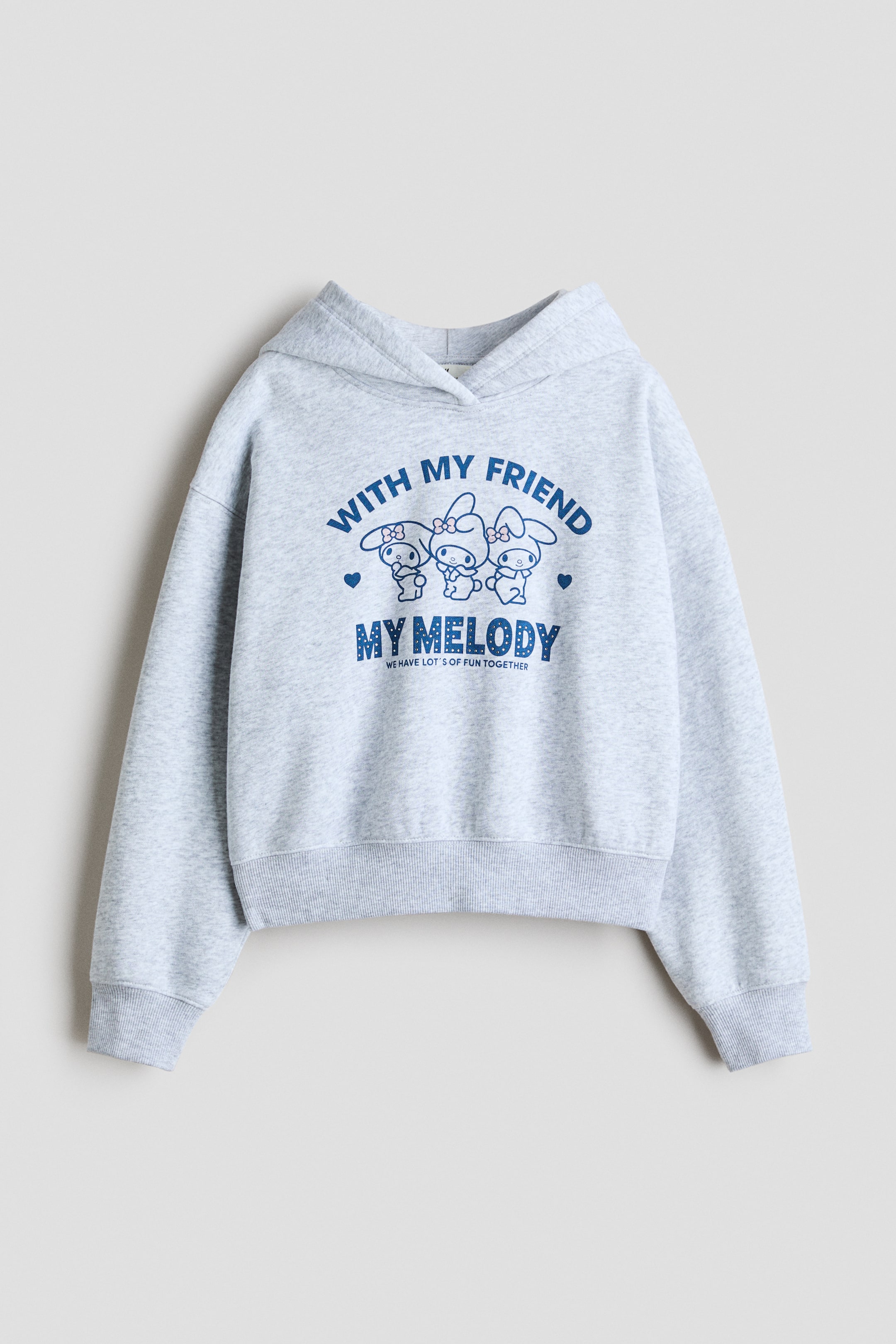Grotere afbeelding bekijken: Een lichtgrijze melange hoodie is van voren weergegeven, met een gewikkelde capuchon aan de voorkant, verlaagde schoudernaden en ribboorden aan de mouwen en zoom. Op de borst staat een blauwe grafische print van stripfiguren met de tekst "WITH MY FRIEND MY MELODY".