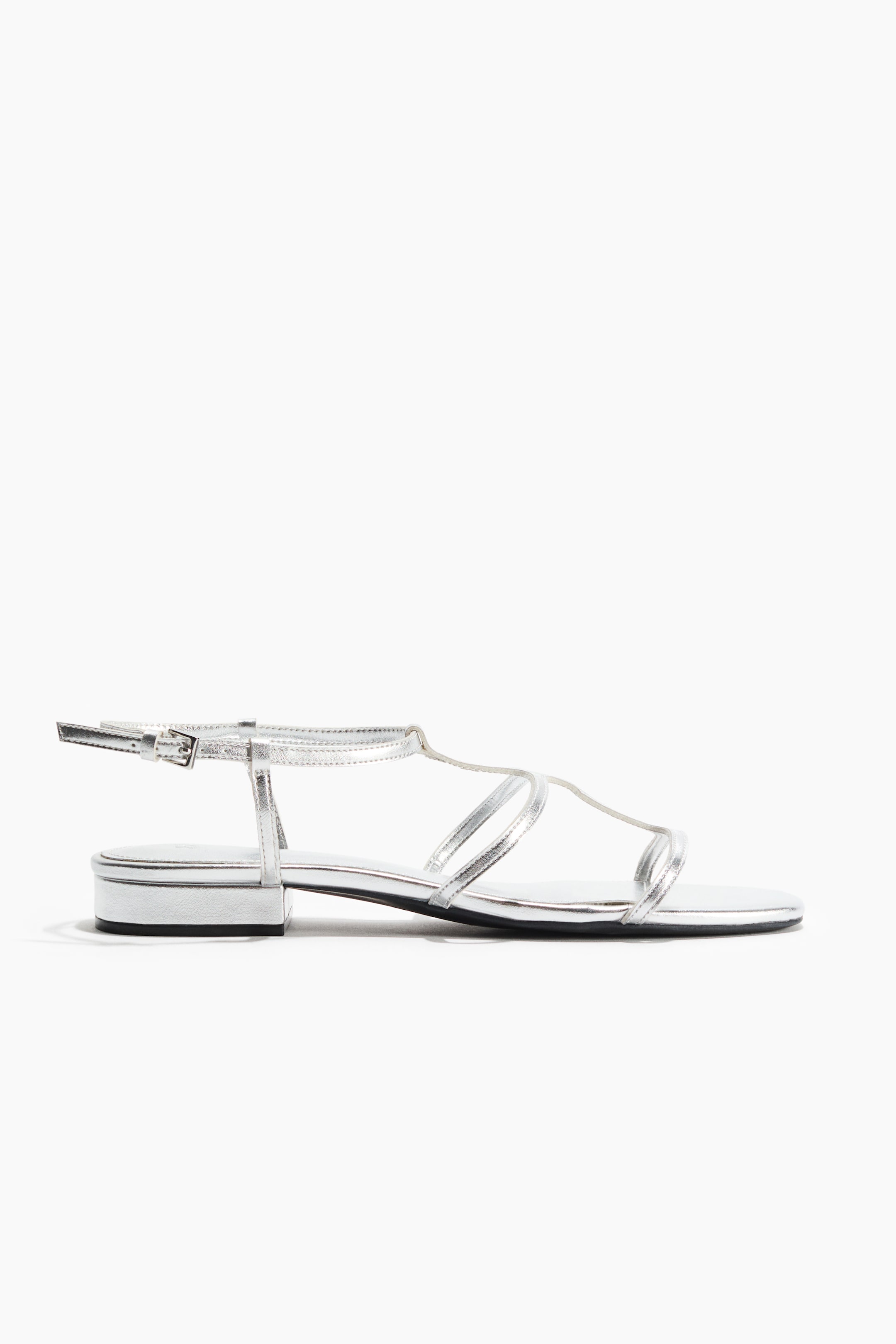 View larger image: The silver metallic sandal showcases a sleek T-strap design across the foot, complemented by an adjustable ankle strap with a buckle. It features a low block heel and a flat sole.