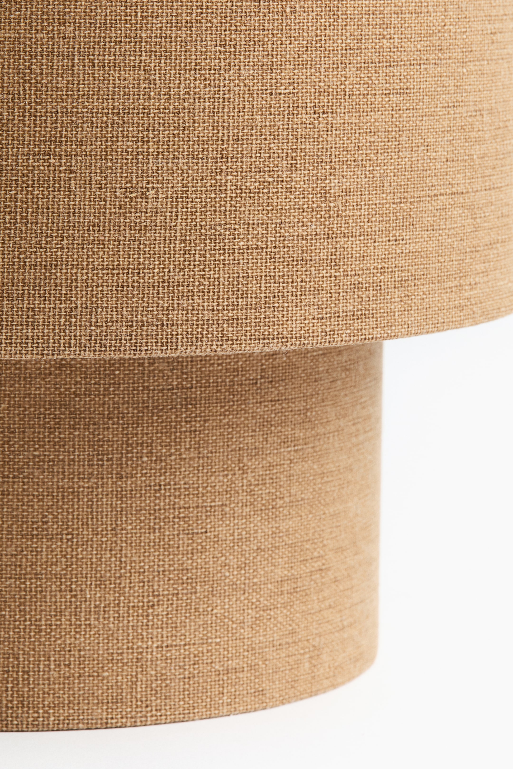 View larger image: A small table lamp showcases its cylindrical shape, featuring a textured light brown woven fabric covering both its base and its slightly wider lampshade.