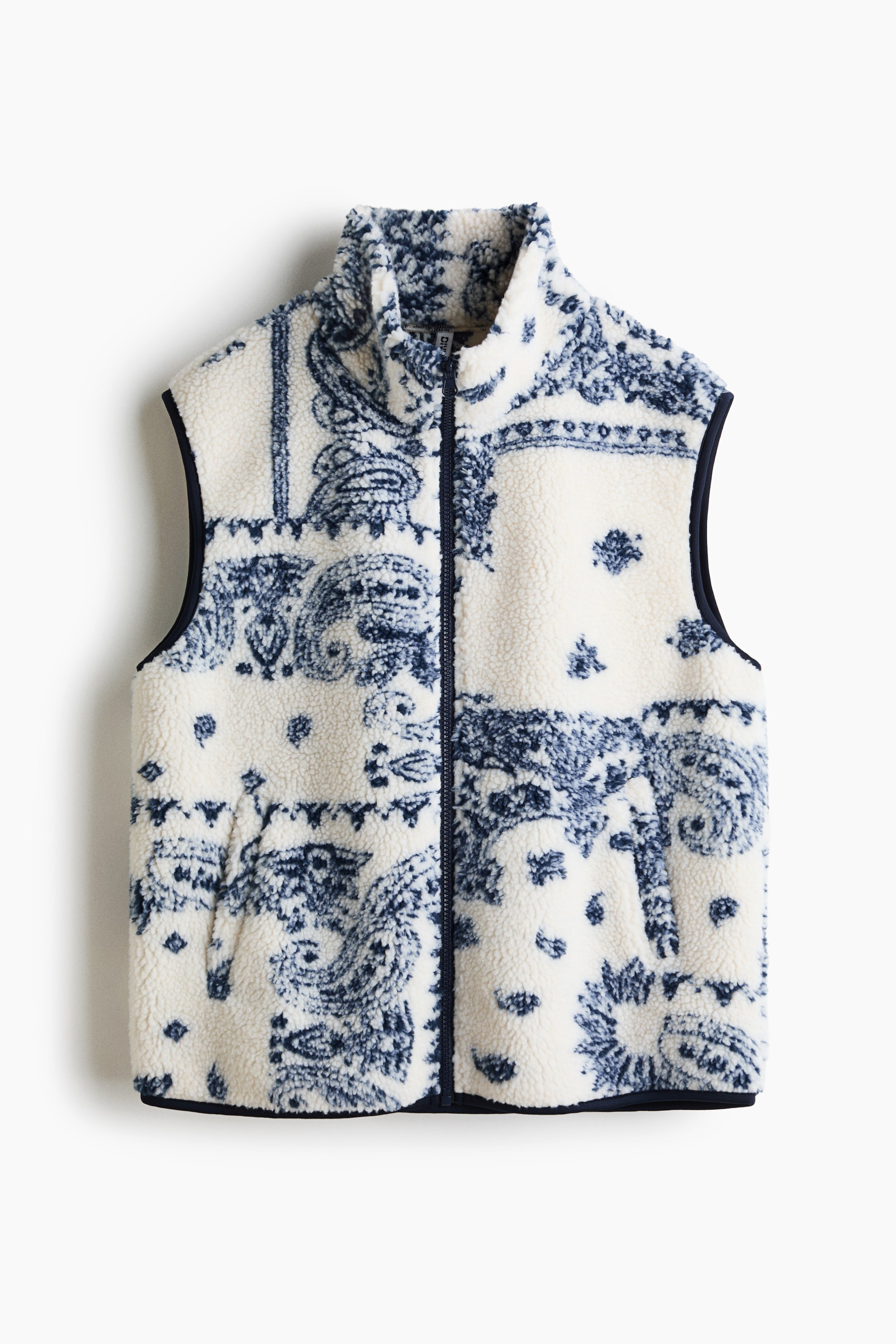 View larger image: A white sherpa fleece vest is shown from the front, featuring an all-over dark blue paisley pattern, a full-zip closure, a stand-up collar, and two vertical welt pockets.