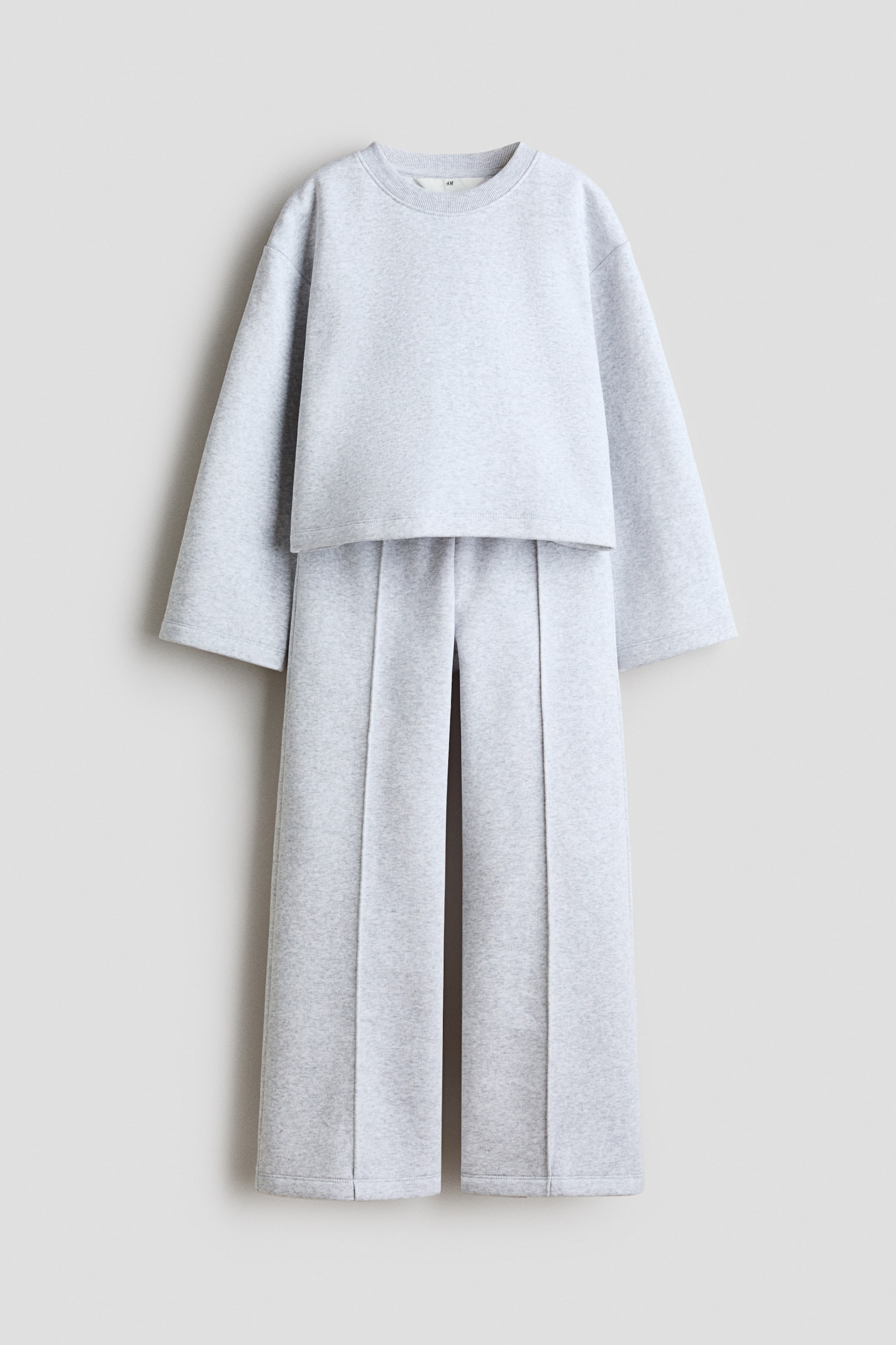 View larger image: A light grey loungewear set is displayed in a front view, consisting of a cropped crew neck top with wide sleeves and matching wide-leg trousers. The trousers feature prominent seams running down the front of each leg.
