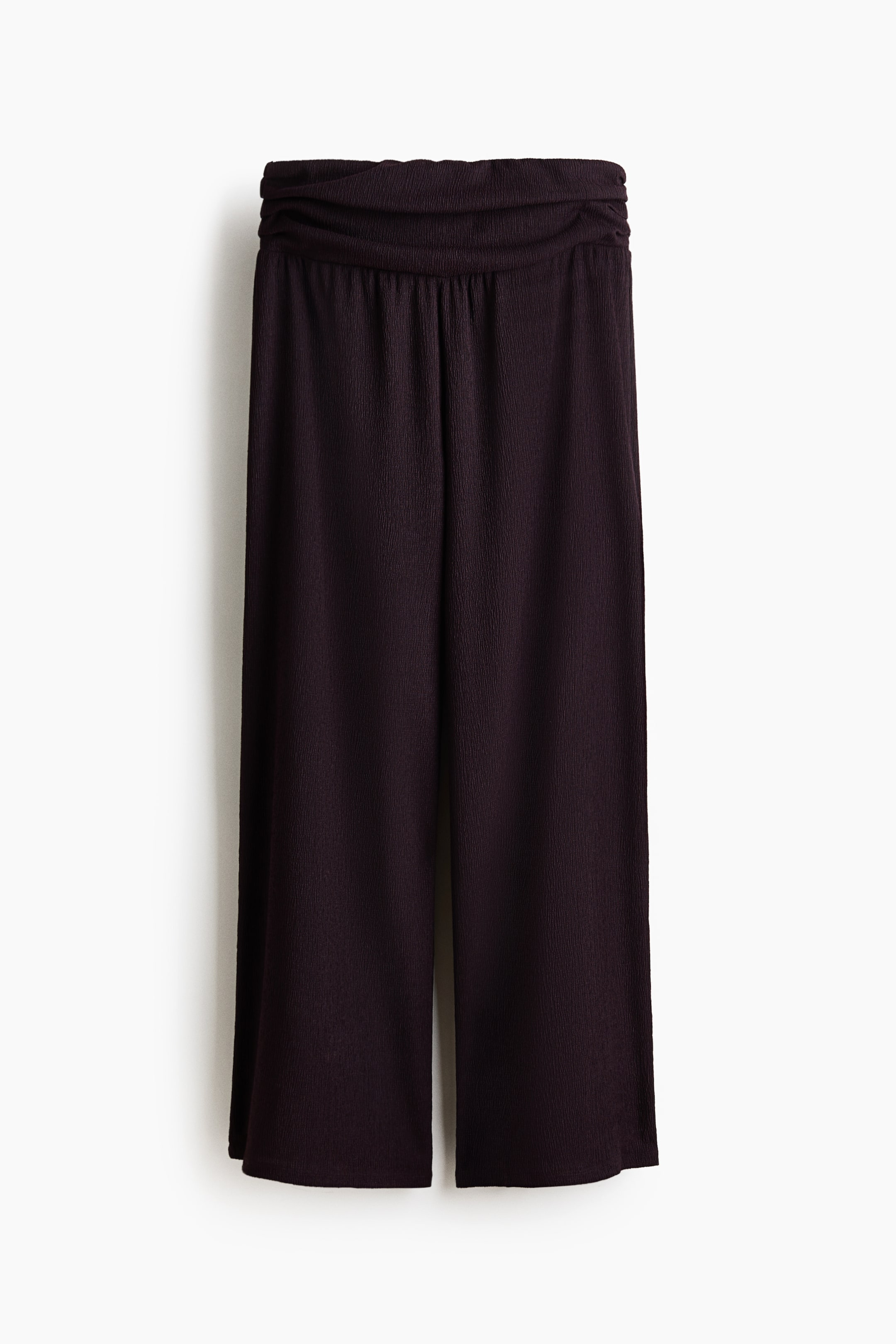 Grösseres Bild ansehen: Weit geschnittene, locker sitzende Hosen sind von vorne zu sehen. Sie zeichnen sich durch eine dunkle, geknitterte Jersey-Textur, eine hohe Taille und einen doppellagigen, gerafften Bund aus.