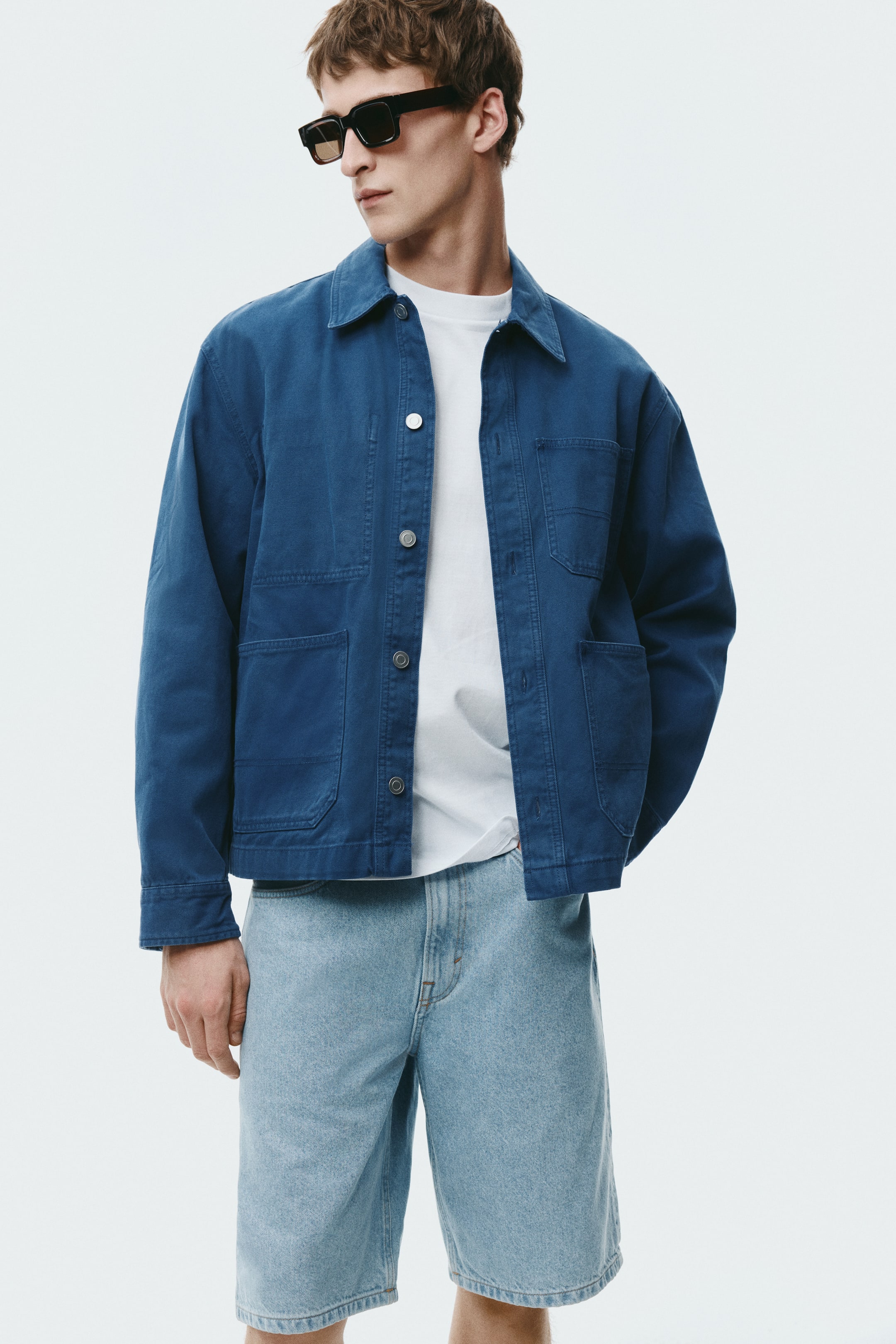 이미지 확대 보기: 모델이 파란색 초어 재킷을 착용하고 있으며, 뾰족한 칼라와 앞면 버튼 여밈, 4개의 패치 포켓이 특징으로 화이트 티셔츠 위에 레이어드되어 있다.