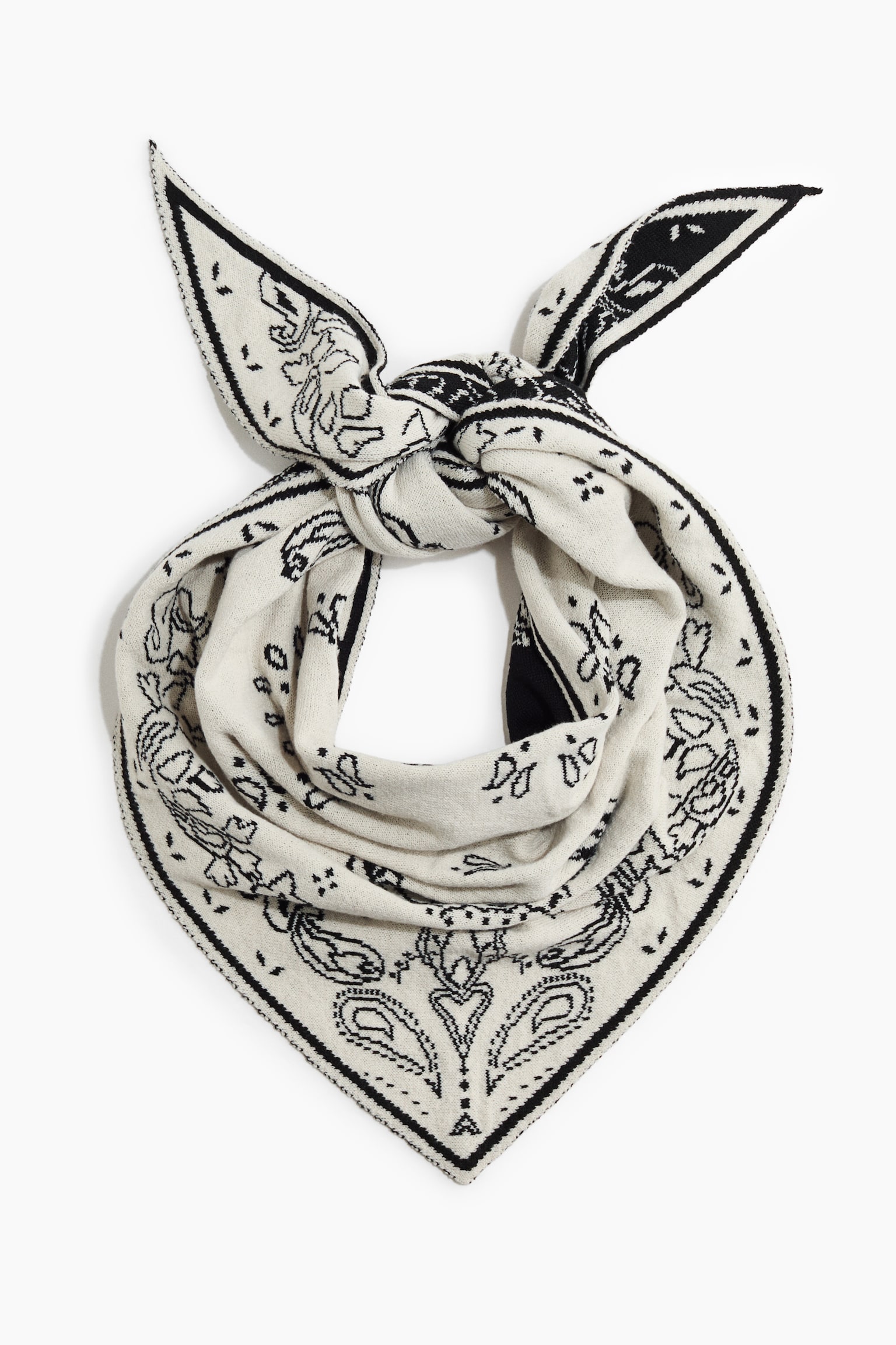 An off-white knit bandana scarf is shown from the front, featuring a black paisley pattern. The scarf is tied in a knot at the top with two pointed ends and drapes down into a triangular shape. - 1