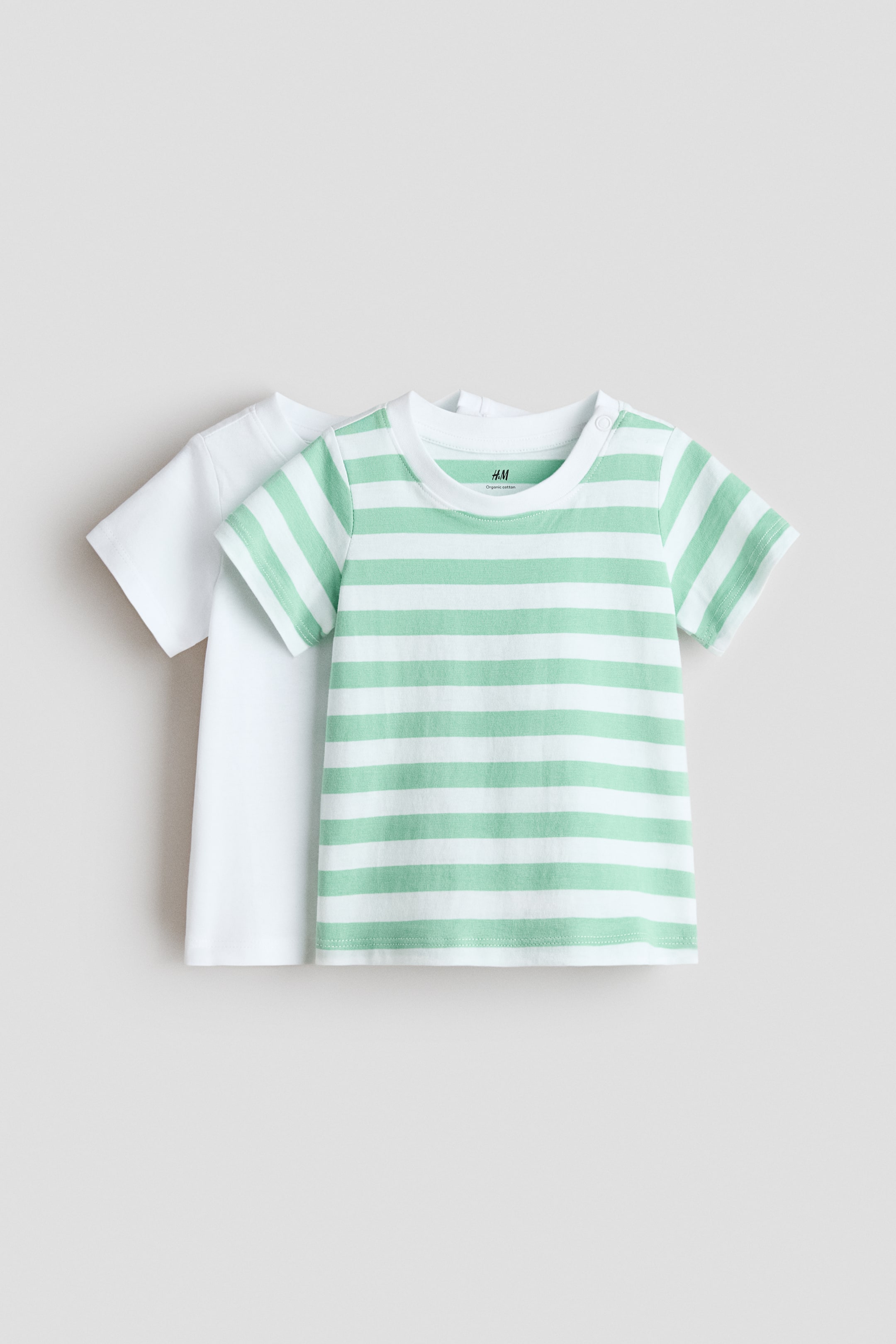 Grotere afbeelding bekijken: 2-pack katoenen T-shirts. Het voorste T-shirt heeft witte en lichtgroene horizontale strepen, een geribde ronde hals en twee drukknoopjes op de linkerschouder. Het tweede T-shirt, iets naar achteren gepositioneerd, is effen wit en heeft ook een geribde ronde hals.