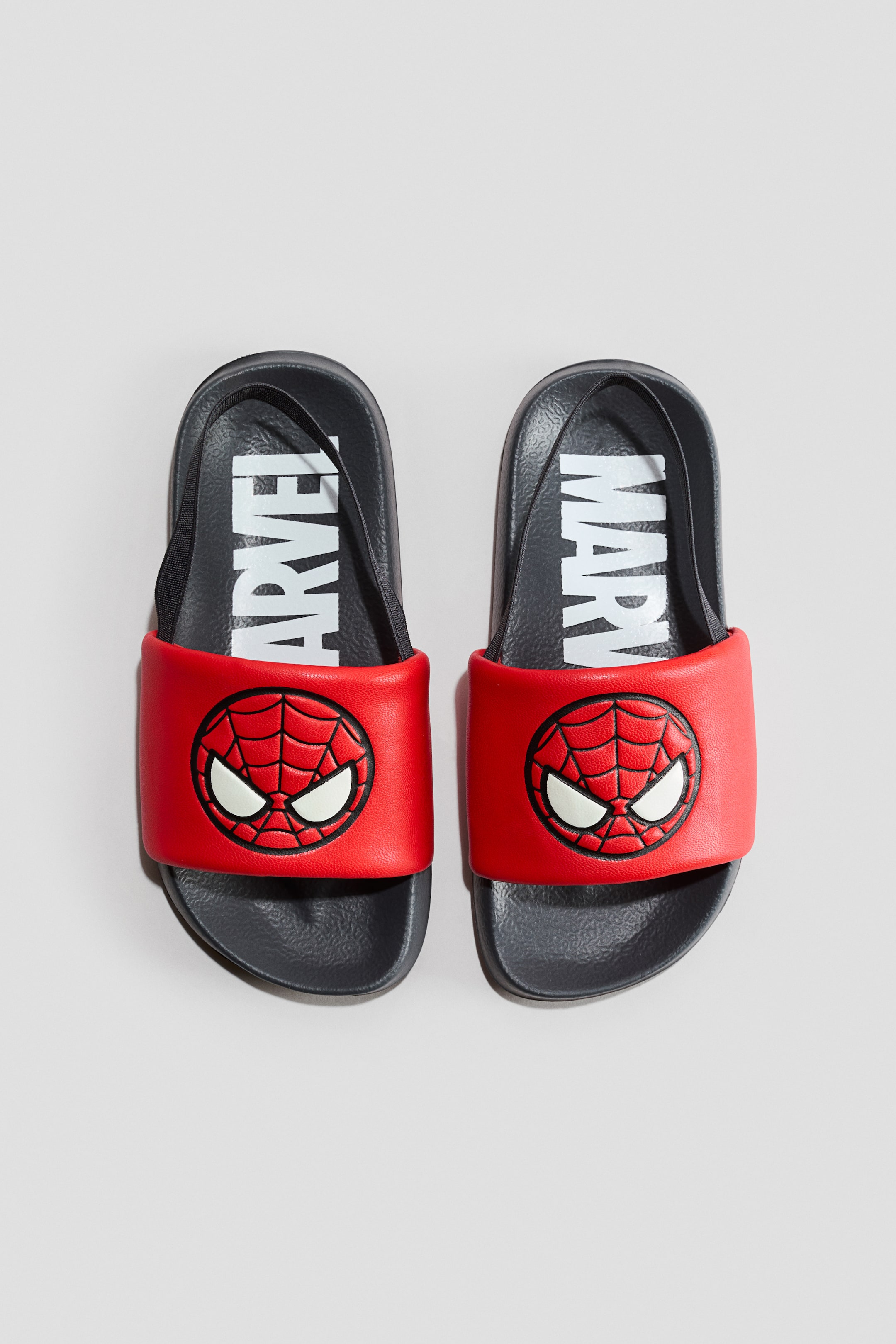 Agrandir l'image: Une paire de chaussures de piscine imprimées avec des semelles moulées gris foncé et des brides rouges ornées d'un graphisme du visage de Spider-Man, présentée de face. Le texte blanc 'MARVEL' apparaît sur la semelle intérieure, et une fine bride élastique noire au talon est également visible.