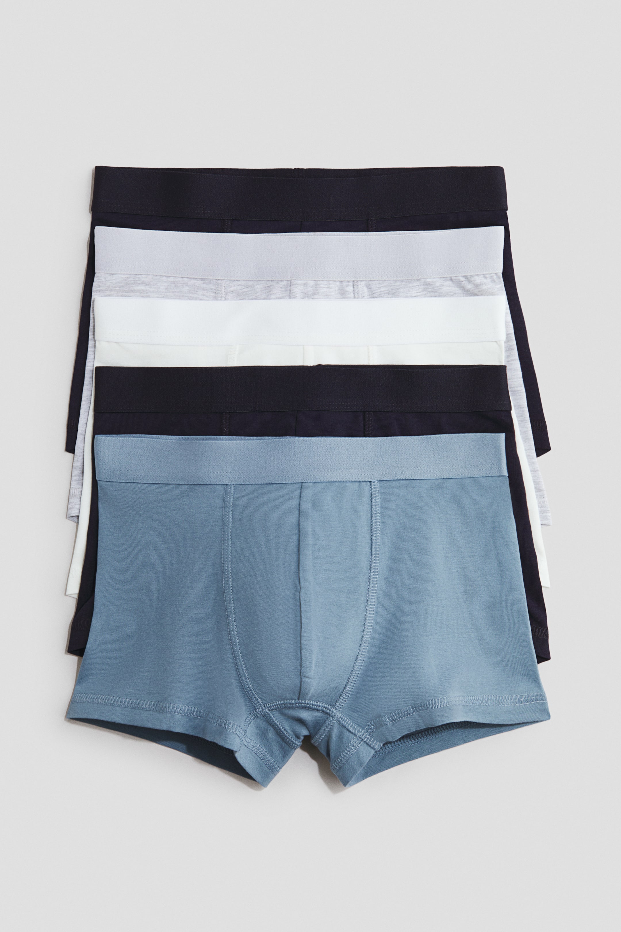 View larger image: Cotton jersey trunks are displayed stacked, showcasing short legs, an elastic waistband, and a lined front. The visible trunks come in a variety of colors such as blue, black, white, and light gray, with their fronts facing forward.