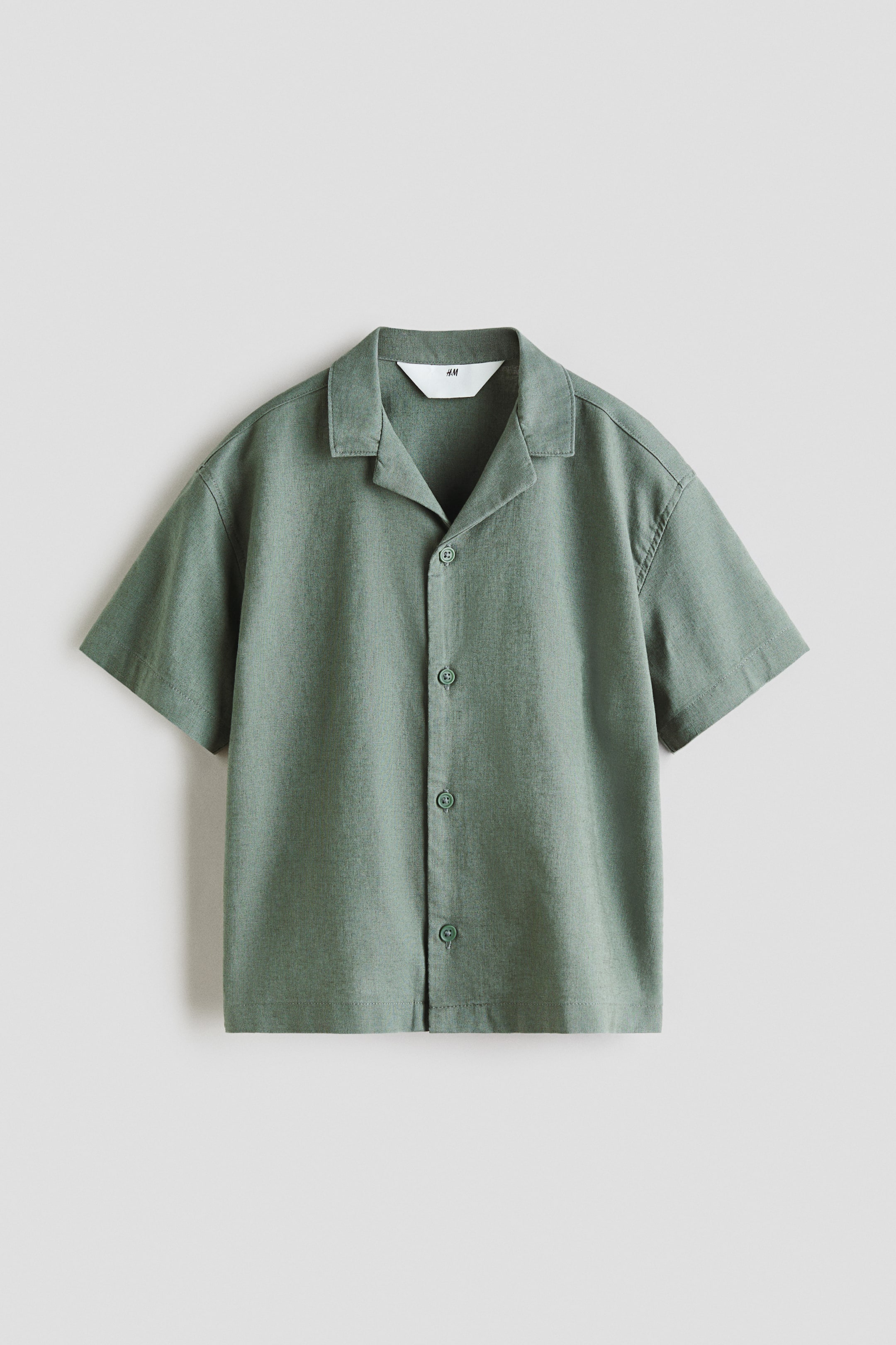View larger image: A short-sleeved shirt in muted green features a camp collar and a full button-down front. Five round, matching green buttons fasten the shirt, offering a relaxed fit from a front-facing angle.