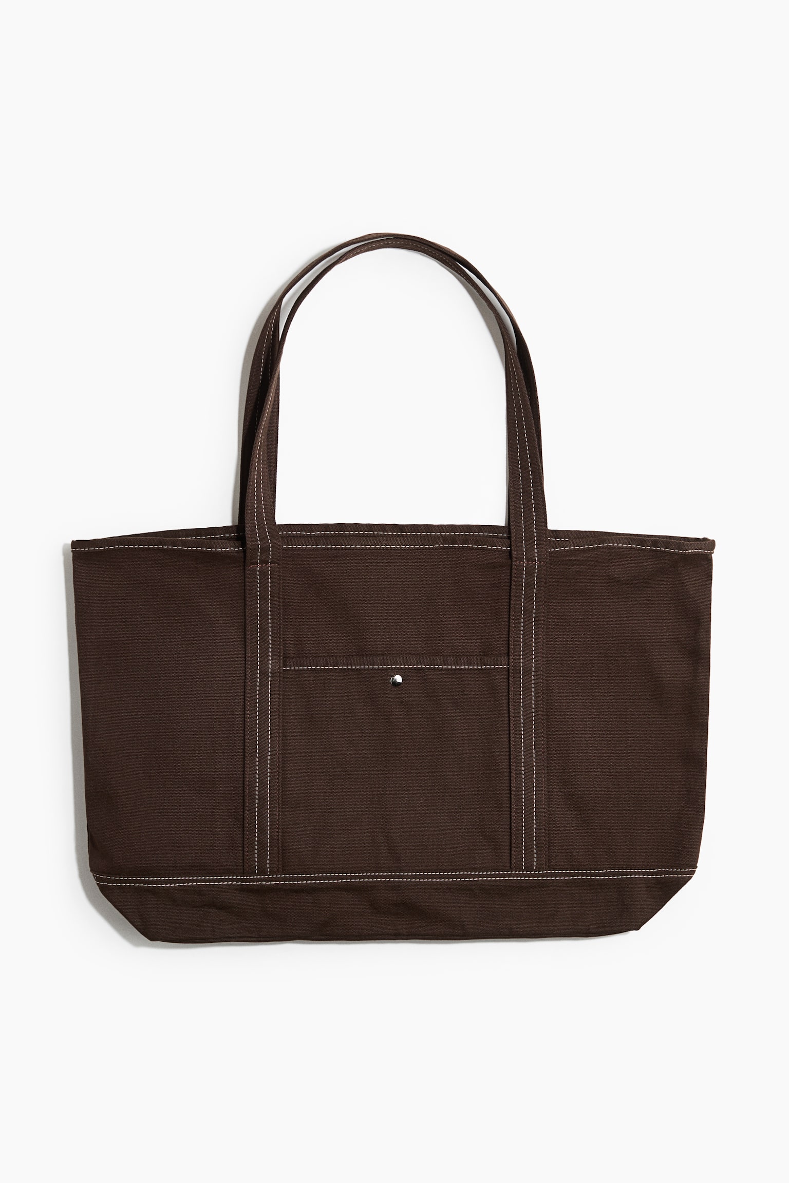 Un sac fourre-tout en coton brun foncé est présenté de face, avec deux poignées supérieures et une poche extérieure avant munie d’une fermeture à pression argentée. Des coutures contrastantes blanches soulignent les coutures, les poignées et les bordures de la poche.