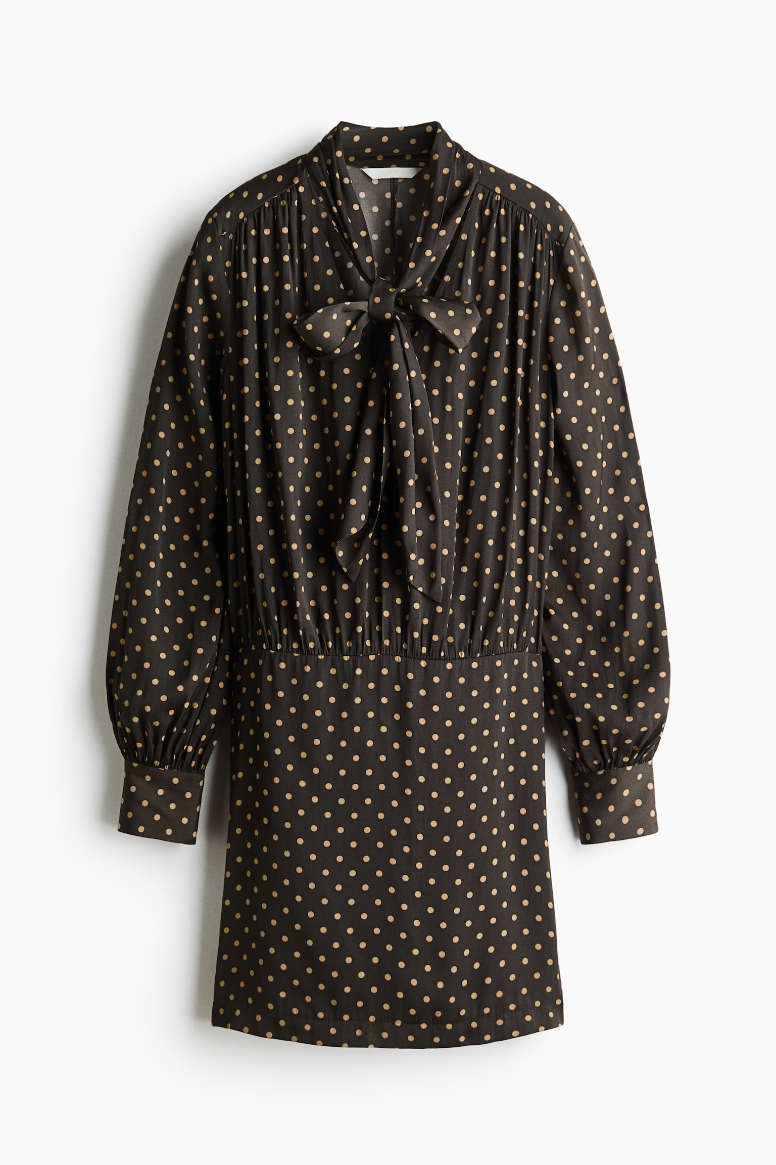 A dark brown mini dress featuring a tan polka-dot pattern is shown from the front. It showcases a high neckline with a self-tie bow, gathered detailing at the shoulders and waist, and long sleeves with wide, buttoned cuffs. - 1