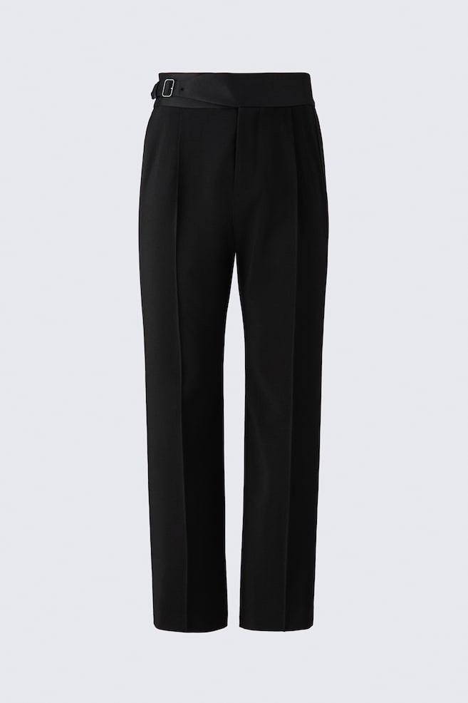 Un pantalon de smoking noir est présenté de face, avec une taille haute recouverte de satin, dotée dâune ceinture latérale intégrée et dâune boucle métallique ton argent. Les jambes à coupe droite affichent des plis marqués au fer le long du centre, de subtils plis sur le devant et des bandes satinées sur les coutures extérieures latérales. - 1