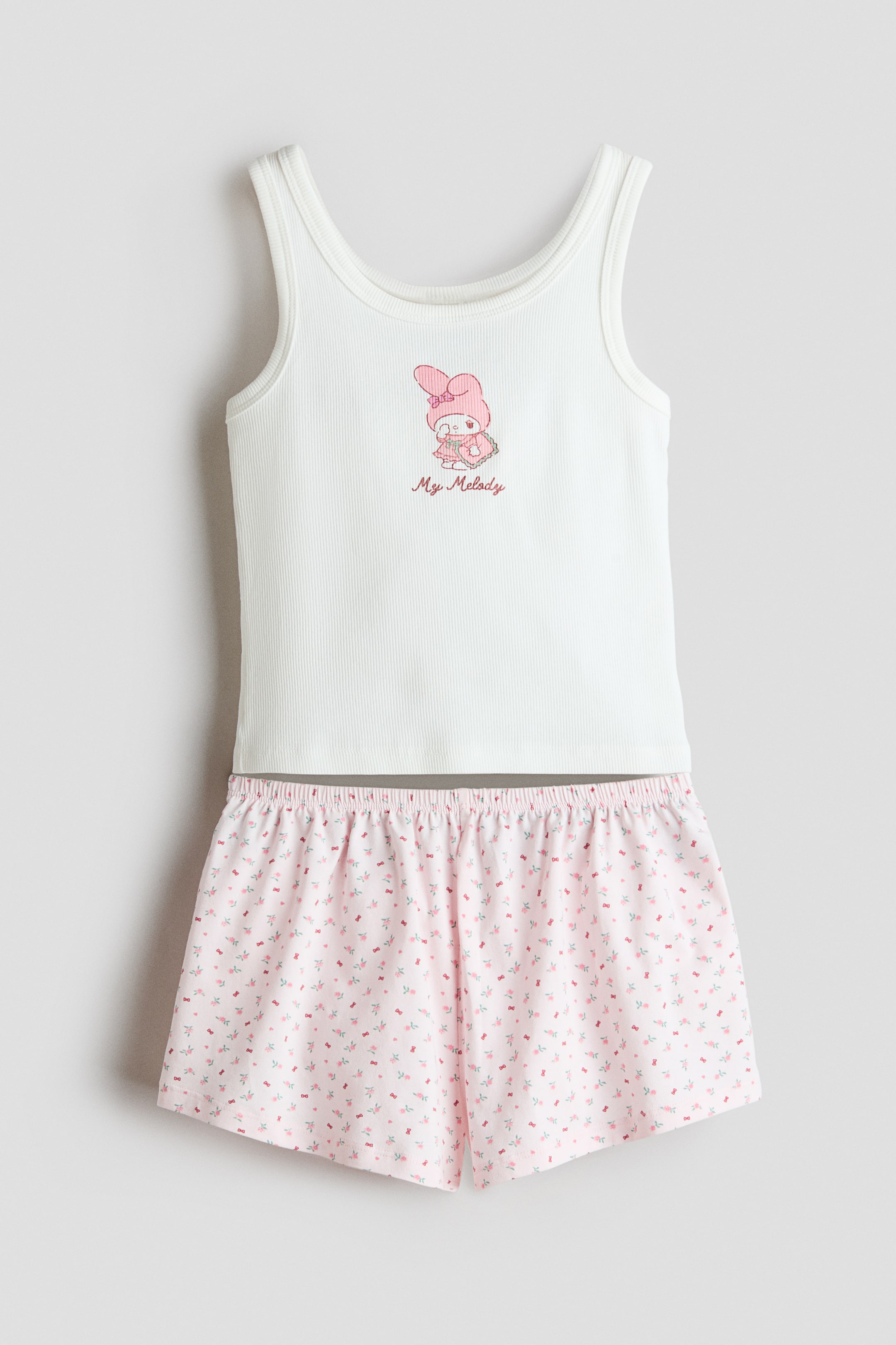 Agrandir l'image: Un ensemble pyjama deux pièces comprenant un débardeur blanc côtelé arborant un graphique du personnage lapin rose et le texte "My Melody" sur le devant. Le short rose présente un imprimé floral et nœud discret, ainsi qu'une taille élastiquée.