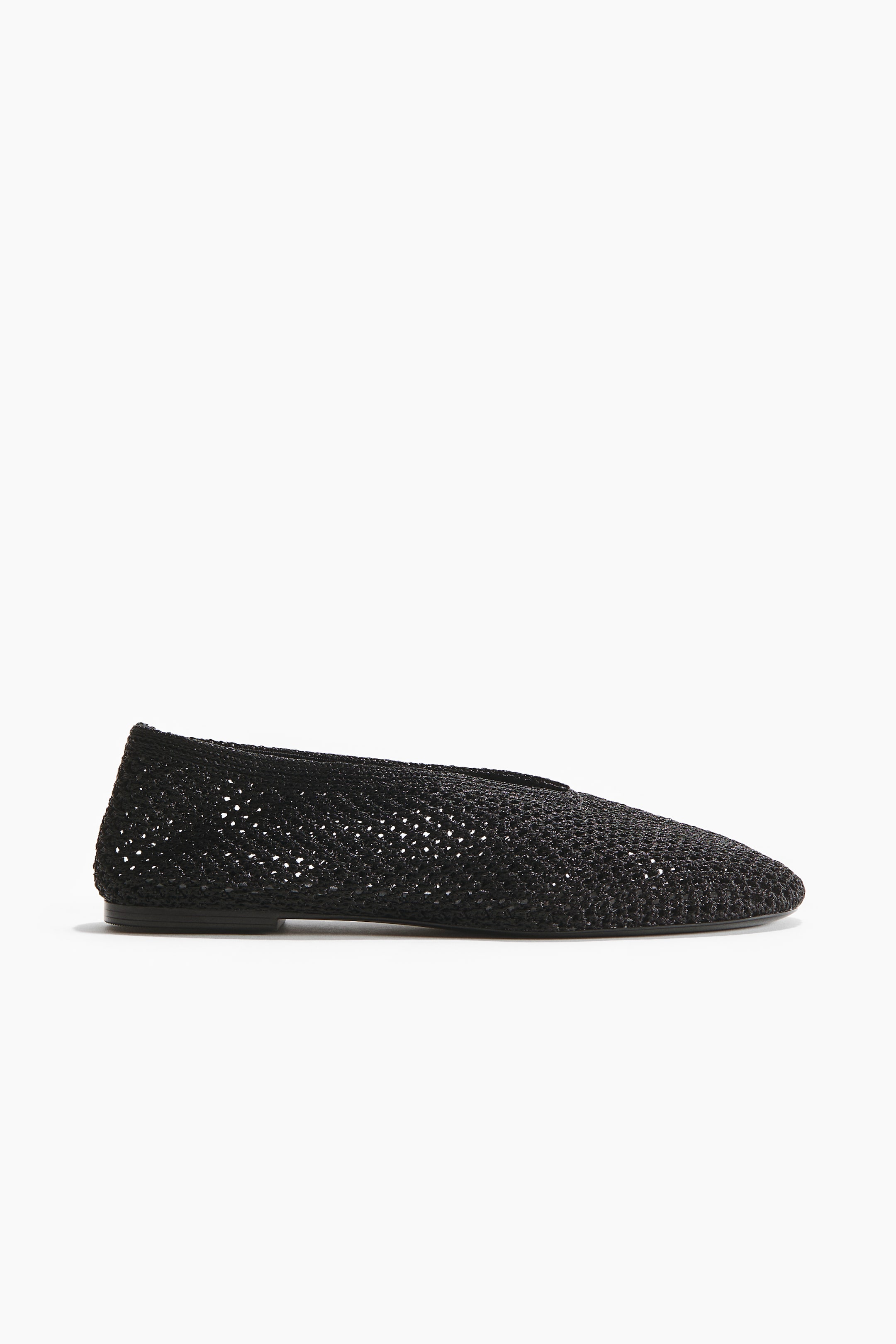 View larger image: A black ballet flat crafted from braided plastic straw showcases a rounded toe and a perforated texture. Displayed from a side view.