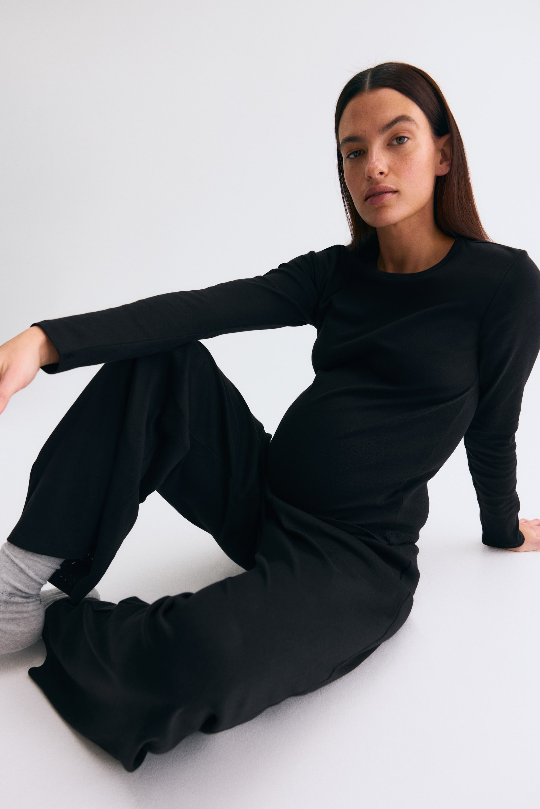 View larger image: A black long-sleeved maternity top features a crew neck and a close fit through the midsection, paired with black wide-leg trousers that drape softly. The trousers have a relaxed fit and fall to the ankles.