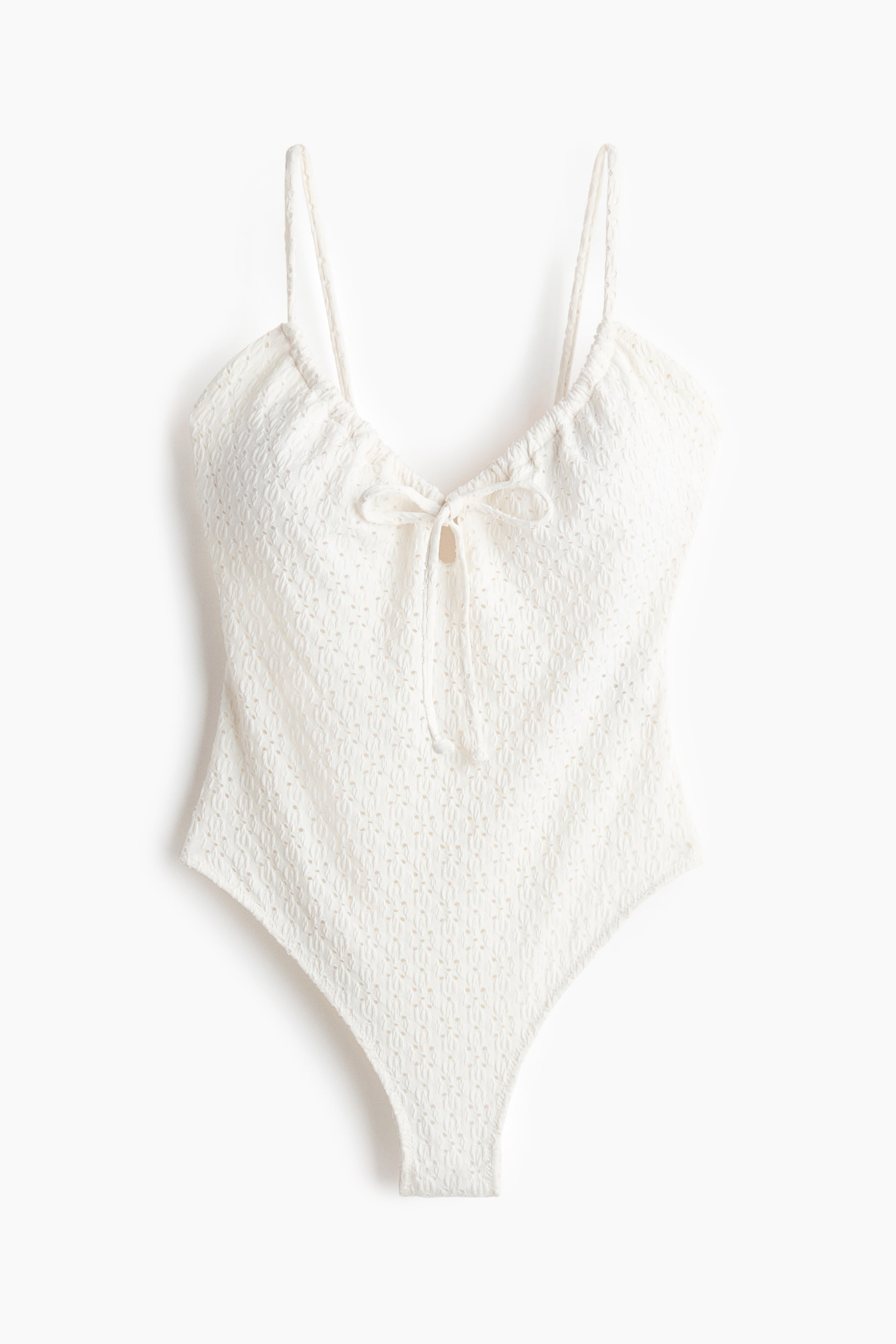 View larger image: A white swimsuit, seen from the front, showcases a textured, all-over pattern, thin spaghetti straps, a gathered neckline with a tie detail at the center front, and high-cut leg openings.