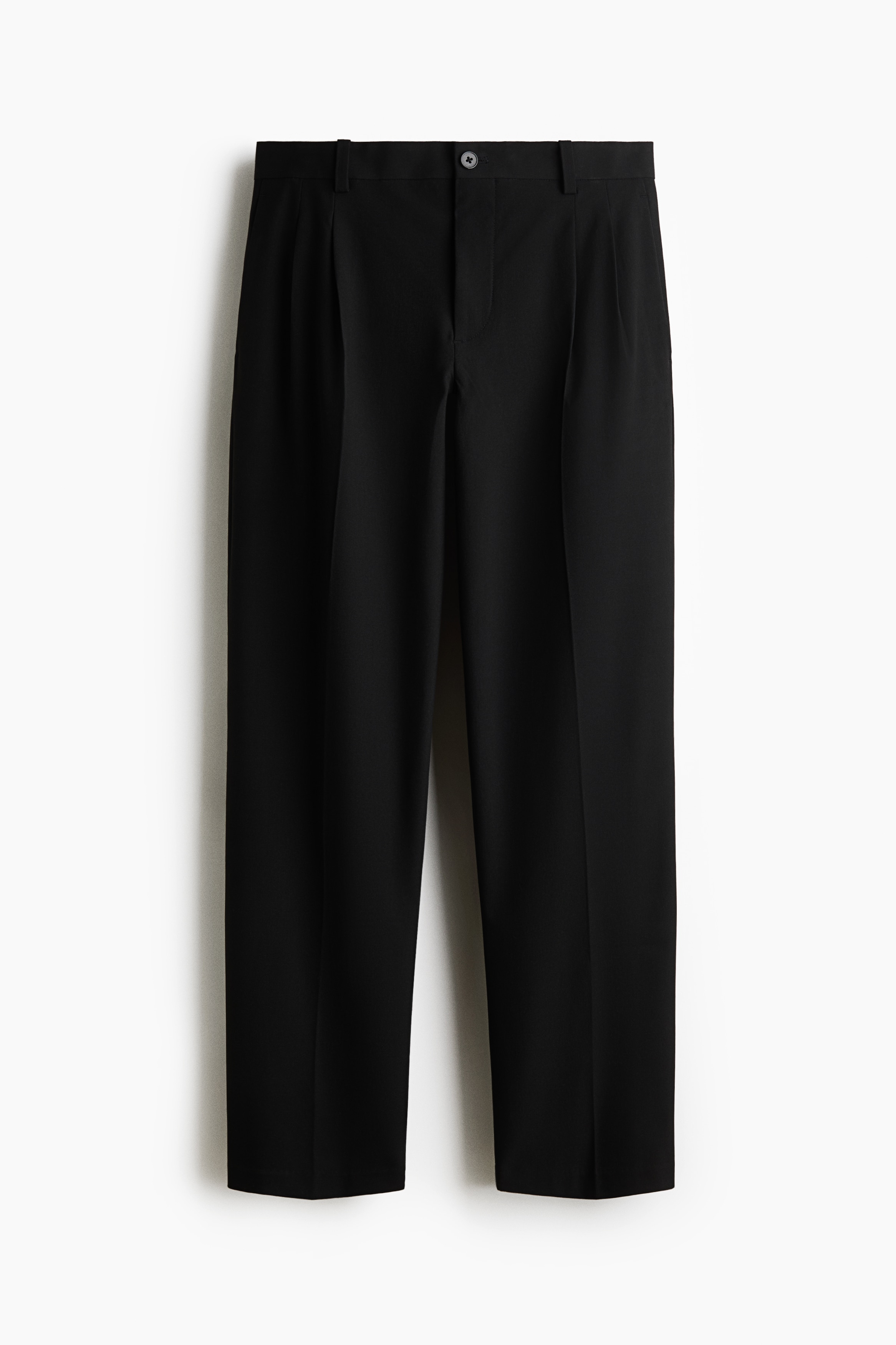Tailored trousers in a dark brown woven fabric are worn by the model, featuring a relaxed fit, straight legs, and sharp front creases. The trousers are styled with a dark crew-neck jumper, a grey double-breasted blazer, and black leather shoes, with the model standing and placing one hand in a side pocket.