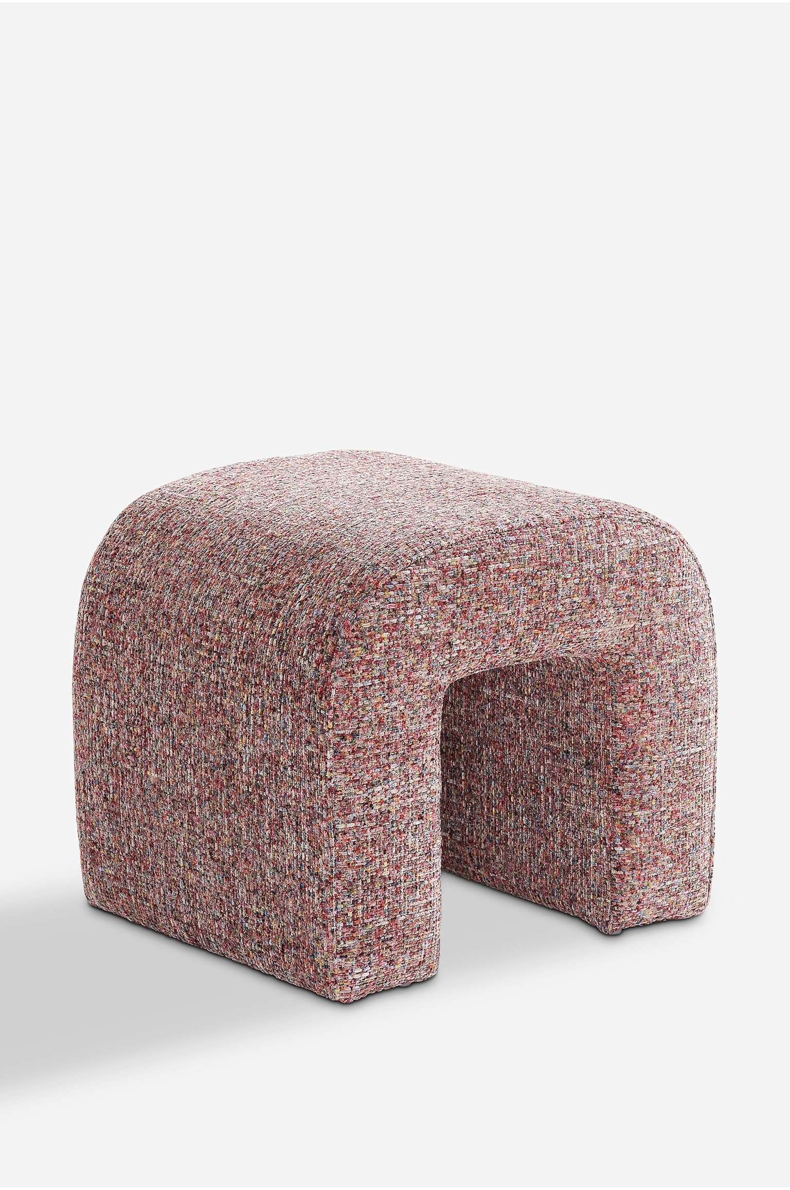 En U-formet puf stÃ¥r i en trekvartvinkel og fremhÃ¦ver sit buede design med afrundet top og hul midte. Skamlen er fuldt betrukket med et tekstureret, flerfarvet vÃ¦vet stof i nuancer af pink, rÃ¸d, gul og creme. - 1
