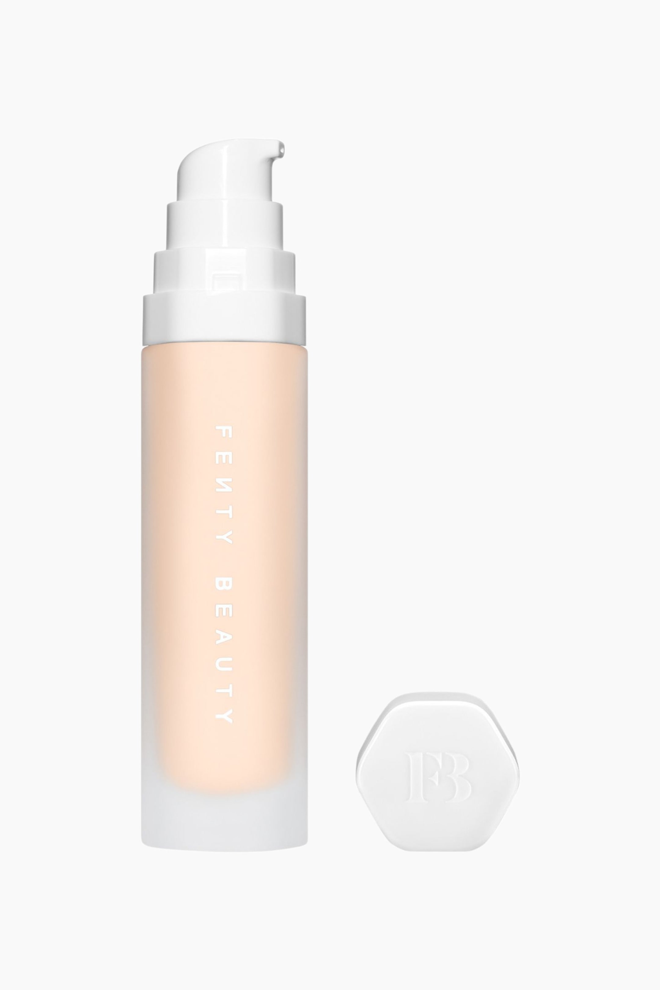 Visa större bild: Soft'lit Naturally Luminous Longwear Foundation står upprätt och visar upp en frostad cylindrisk flaska fylld med en ljus persikofärgad vätska samt vertikal märkning med "FENTY BEAUTY". En vit pumpdispenser sitter ovanpå flaskan, och en separat sexkantig vit kork med en präglad "FB"-logotyp vilar bredvid basen.