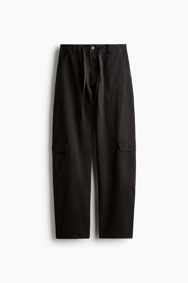 Schwarze Cargo-Hose aus Baumwoll-Twill, von vorne gezeigt, mit Kordelzugbund, Knopfverschluss und GÃ¼rtelschlaufen. Die Hose verfÃ¼gt Ã¼ber groÃe aufgesetzte Vordertaschen sowie jeweils eine Blasebalg-Klappentasche an jedem Bein. - 1