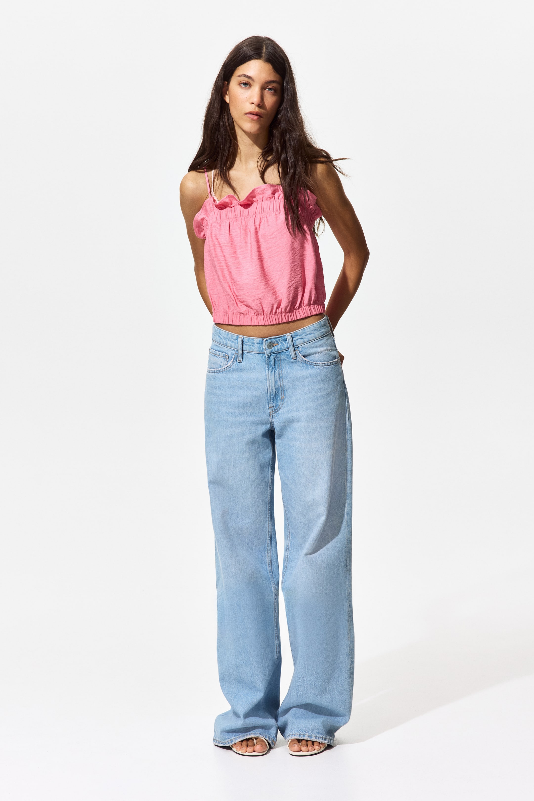 View larger image: "A pink crinkled crop top with a ruffled neckline and spaghetti straps is paired with light blue, wide-leg jeans showcasing a faded wash and standard pockets, both shown from a front-facing view."