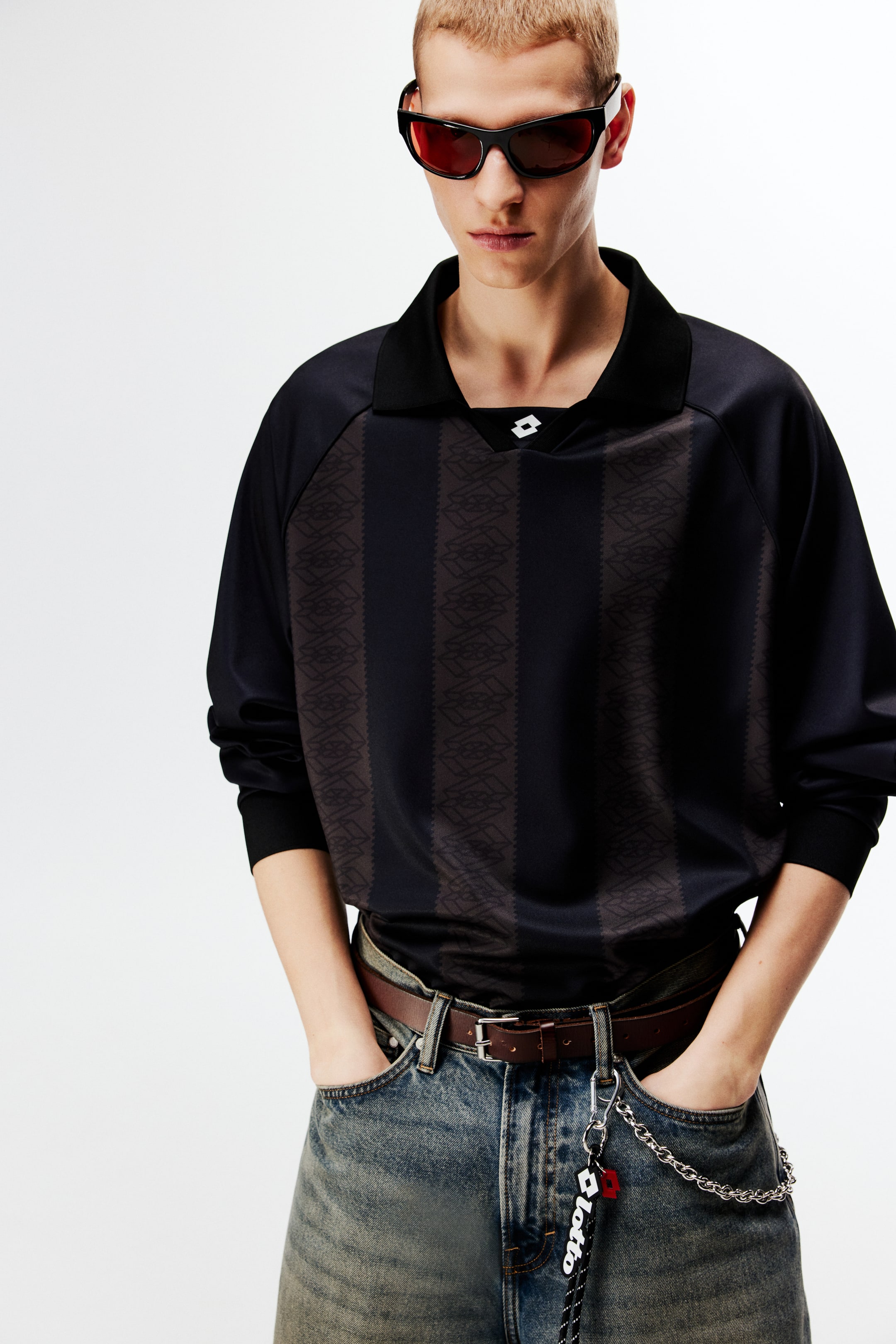 View larger image: A black long-sleeved jersey is being worn, featuring a black polo collar and a V-neck with a white logo. The jersey showcases alternating vertical stripes of solid black and dark grey with an embossed geometric pattern.