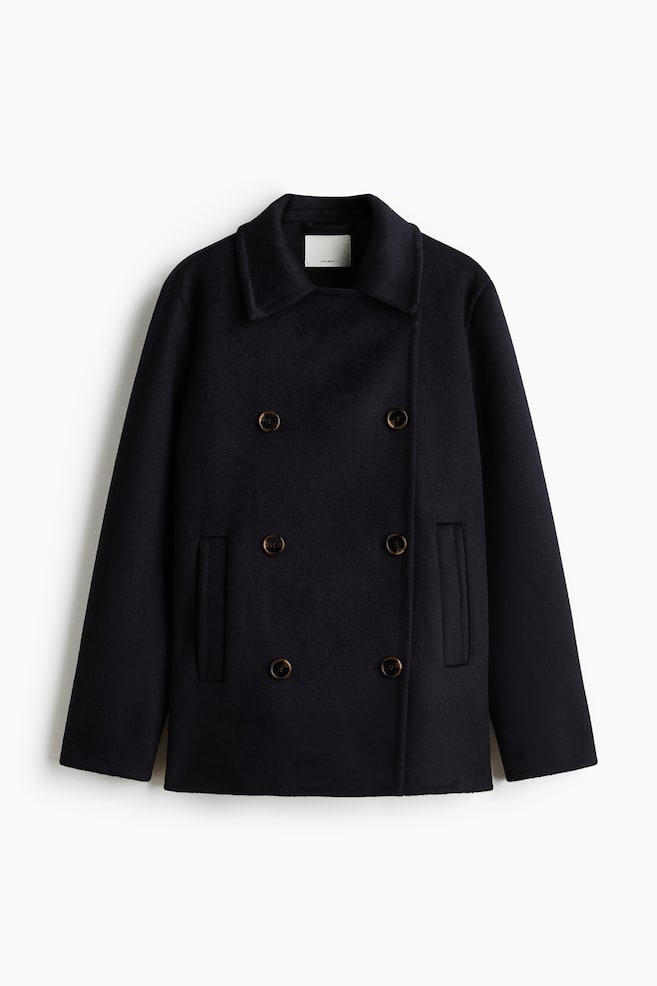 A short, dark navy wool-blend coat is shown facing front, featuring a double-breasted closure with six brown buttons and notch lapels. It is displaying vertical welt pockets on each side and a soft, felted fabric texture. - 1
