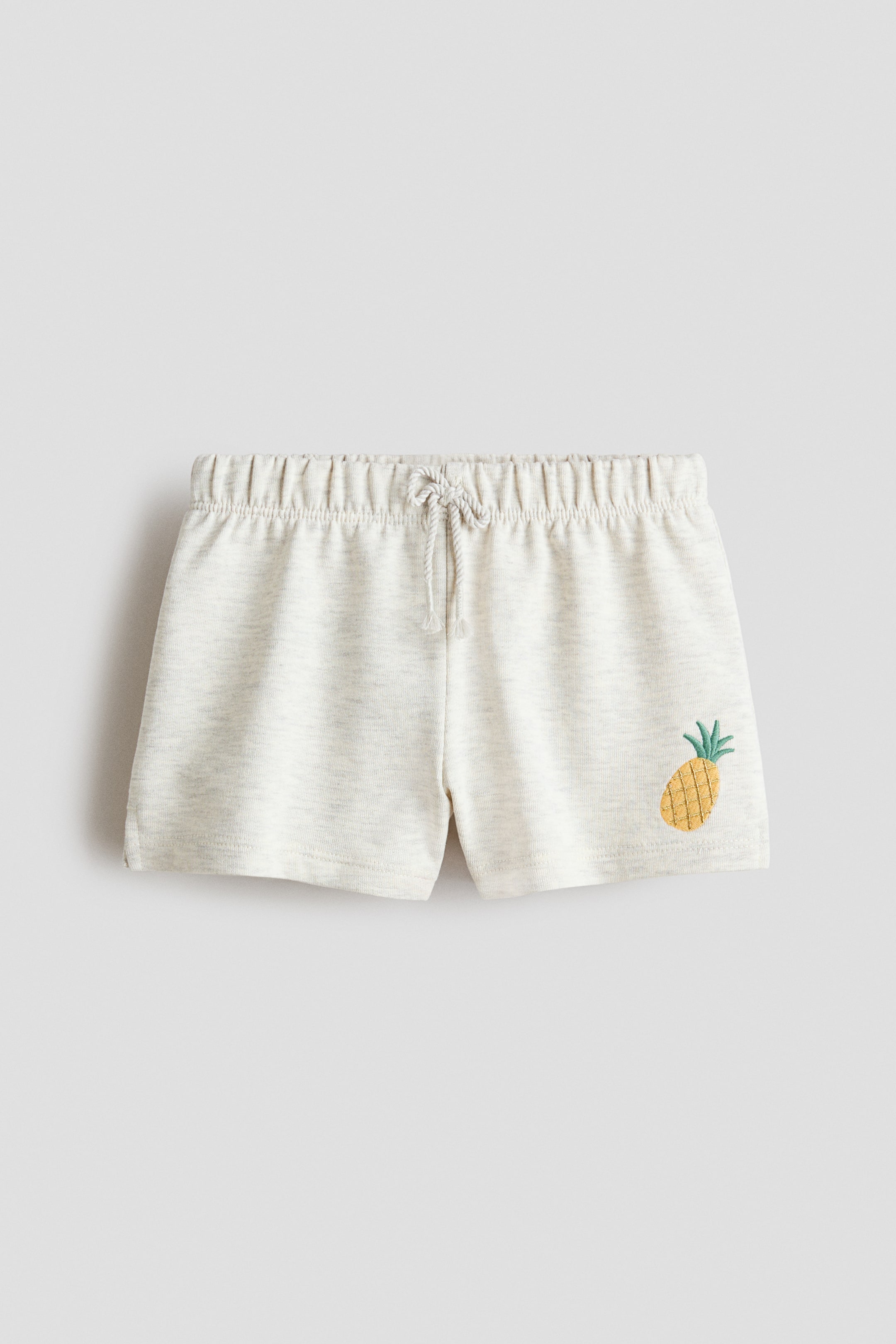 Vis større bilde: Lysegrå melerte sweatshirt-shorts vises forfra, med en elastisk midje og en dekorativ snor. Et lite brodert ananasmotiv er plassert på nedre høyre ben, og subtile splitter er synlige ved kantene.