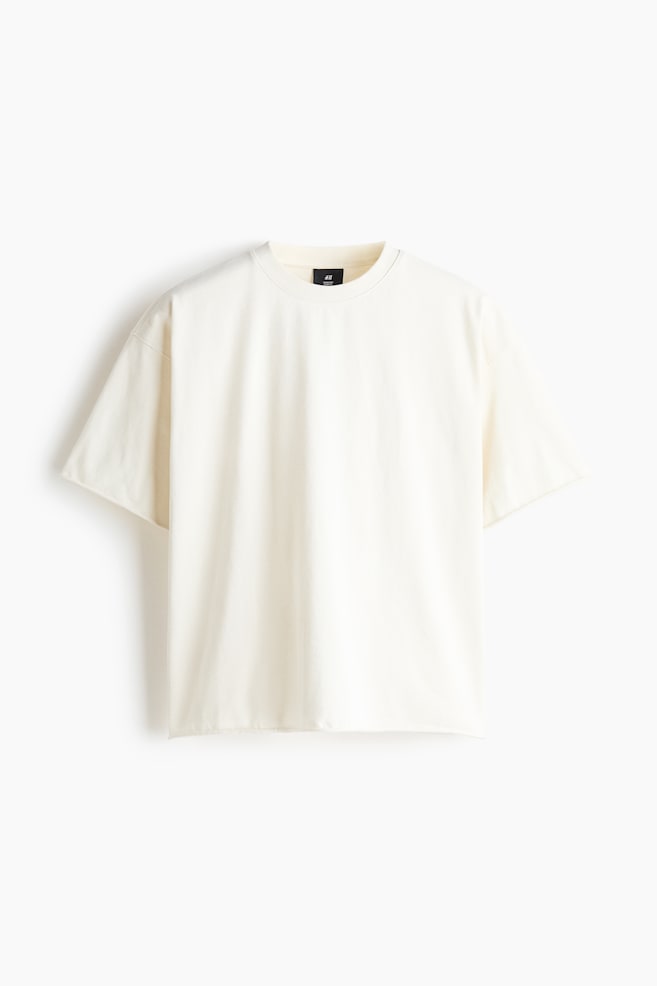 An off-white t-shirt is facing front, displaying a relaxed fit with dropped shoulders and a ribbed crew neck. The garment is featuring wide short sleeves and a straight hem. - 1