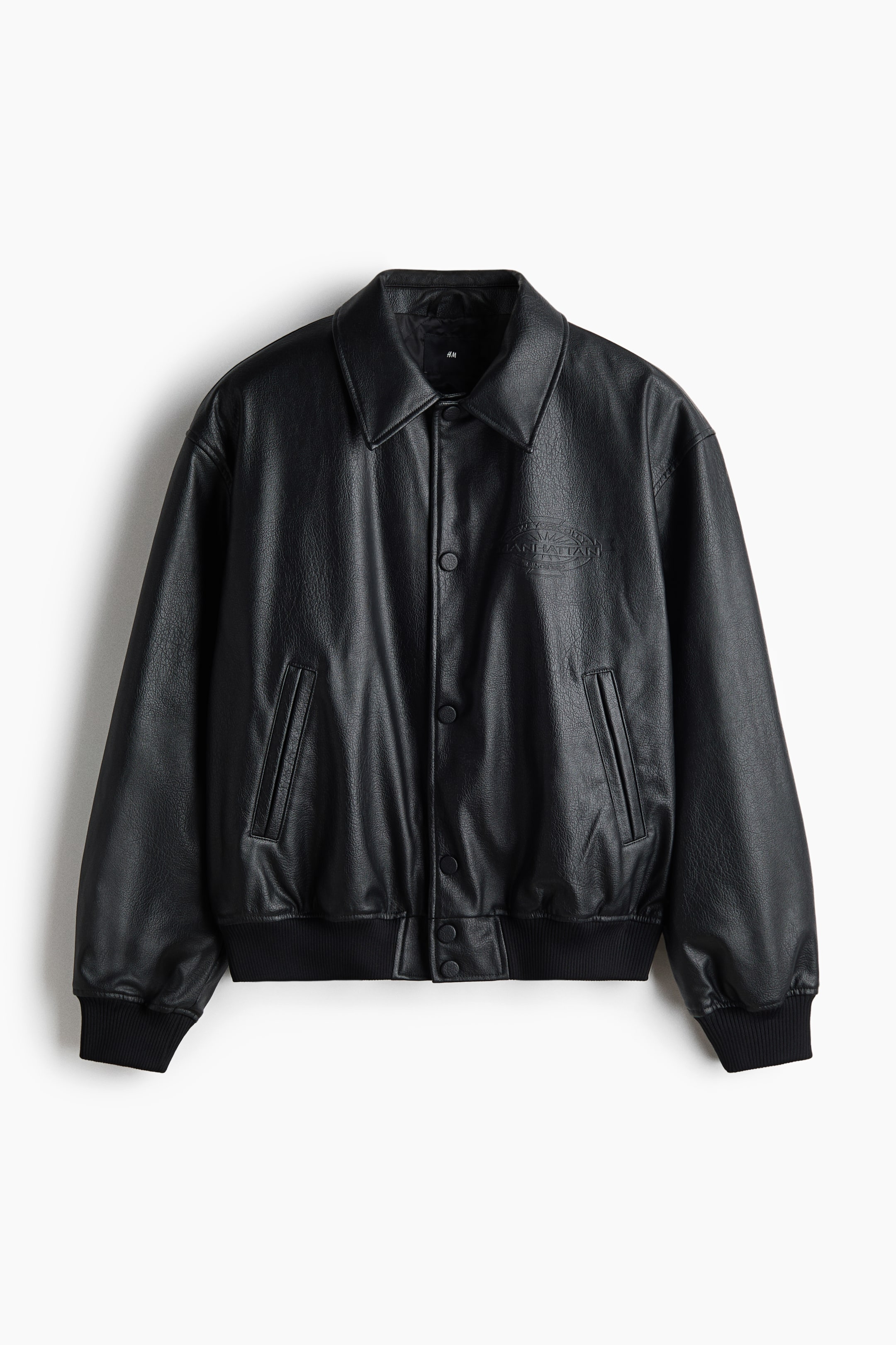 View larger image: A black faux leather bomber jacket is showcasing its front, highlighting a pointed collar, a snap button closure, two front welt pockets, ribbed cuffs and hem, and an embossed "MANHATTAN NEW YORK" graphic on the right chest.