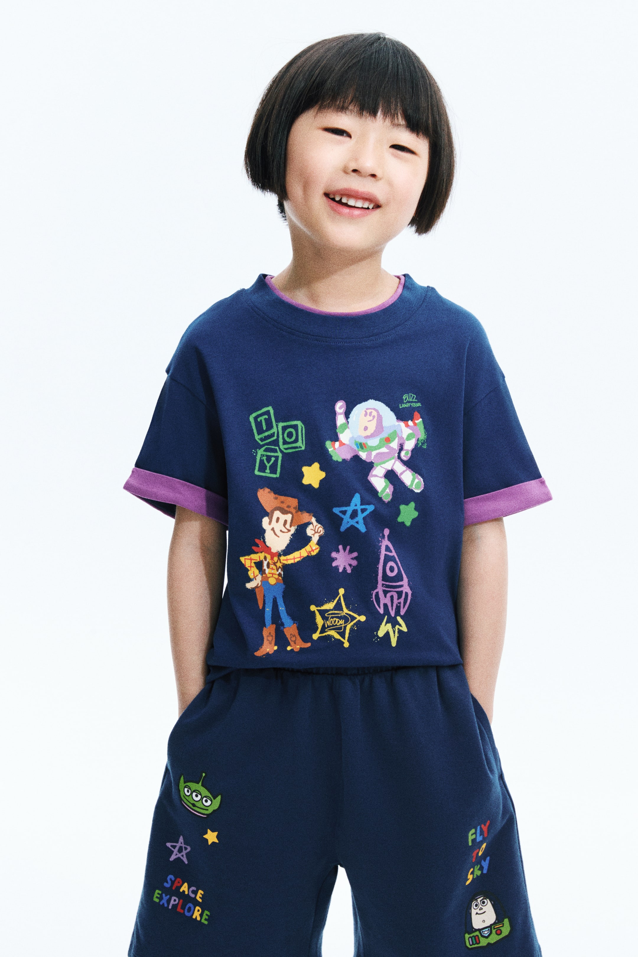View larger image: Presenting a navy blue t-shirt and matching shorts set in a front-facing view, both adorned with vibrant Toy Story graphics. The t-shirt highlights a crew neck with purple trim and short sleeves with purple cuffs, featuring Woody, Buzz Lightyear, a rocket, and stars. The shorts come with an elasticated waistband, side pockets, an alien, Buzz Lightyear, and text that reads 'SPACE EXPLORE' and 'FLY TO SKY'.